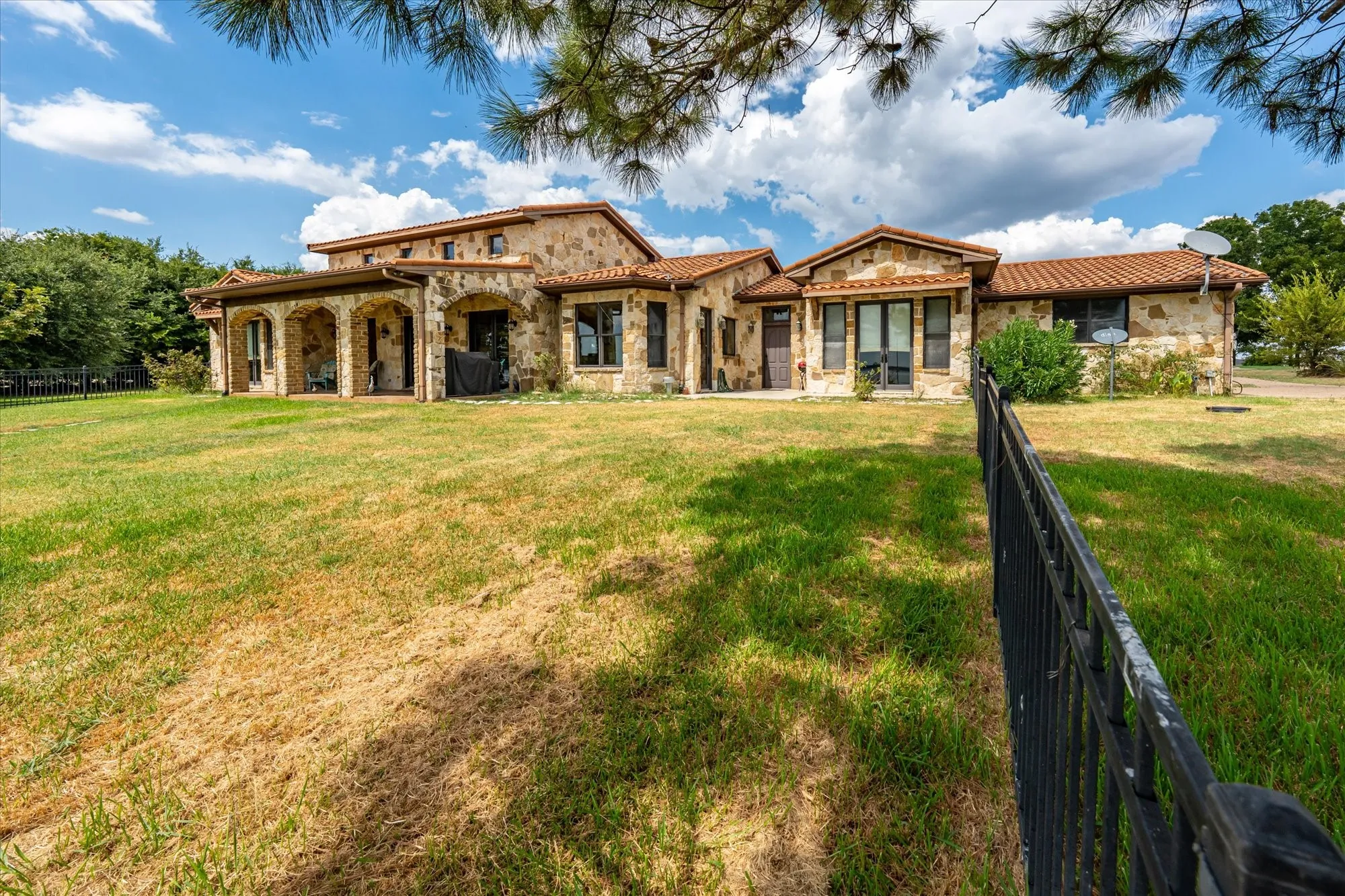 Stone exterior featuring arched patio openings, a tile roof, and multiple windows