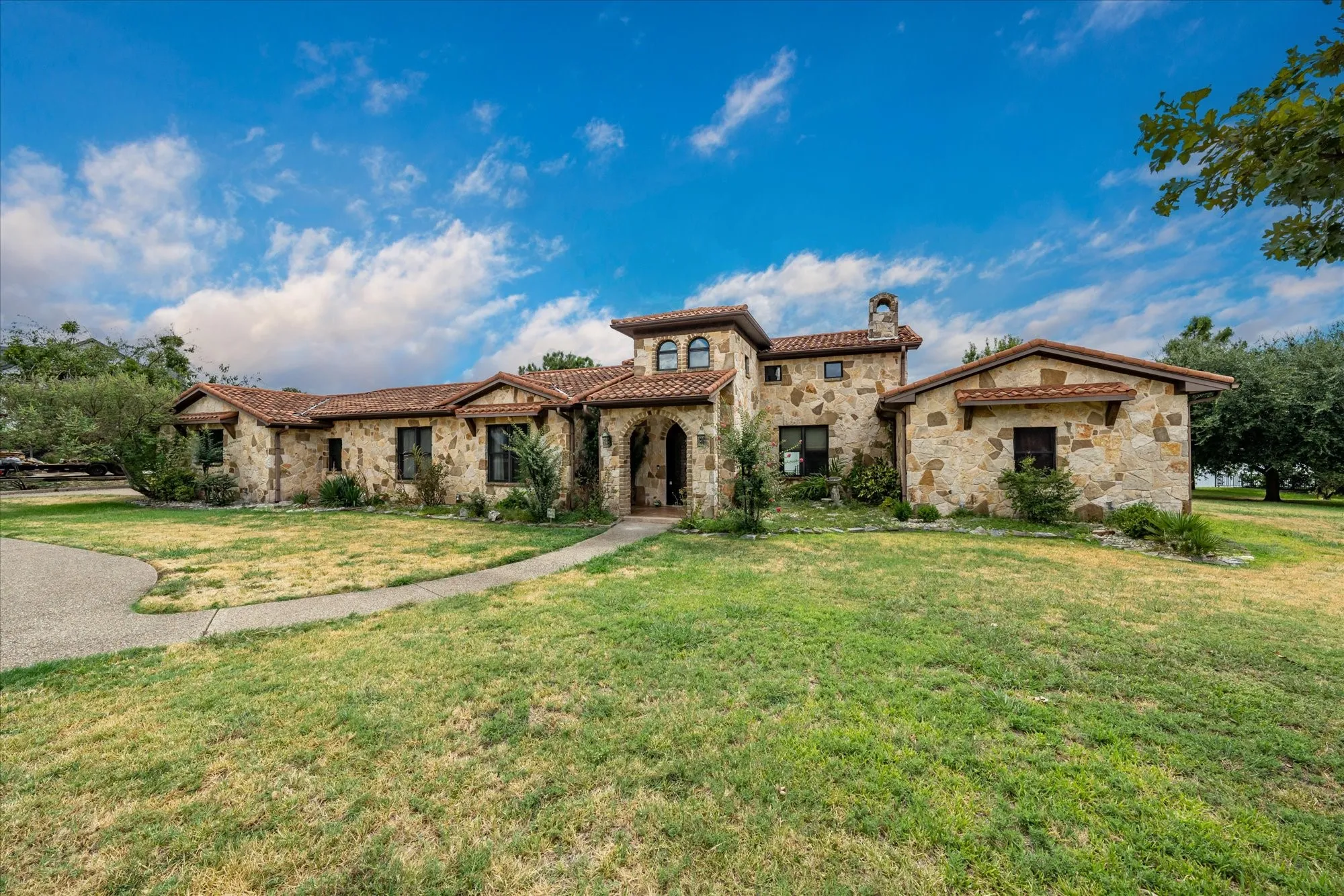 Stone exterior with arched entry, tile roof, and a chimney feature