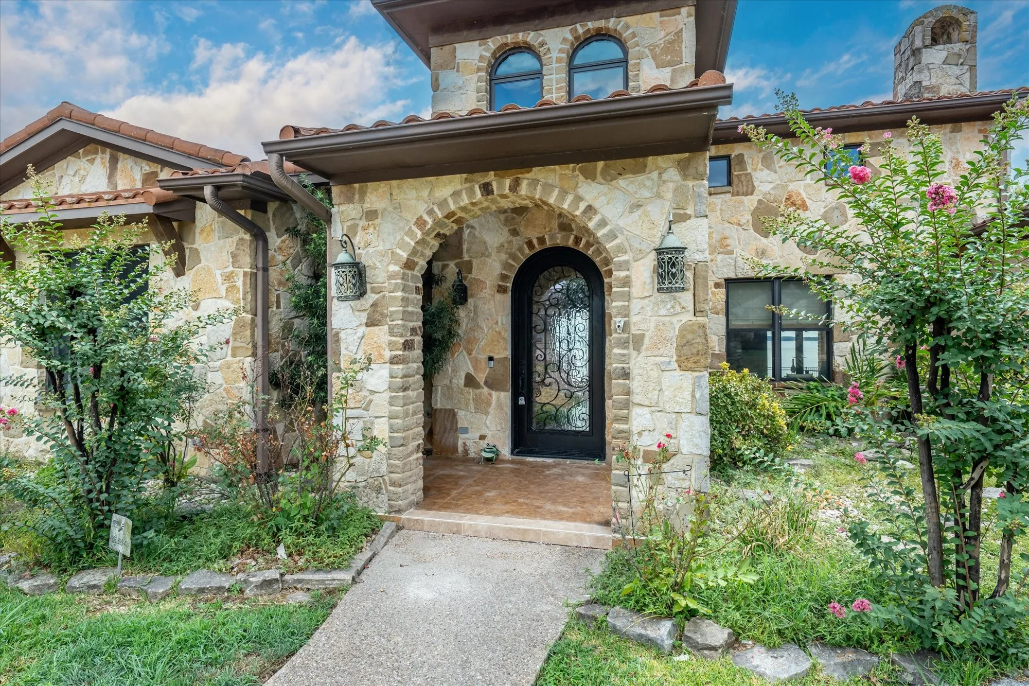 Stone exterior with arched entryway, decorative iron front door, and tiled roof