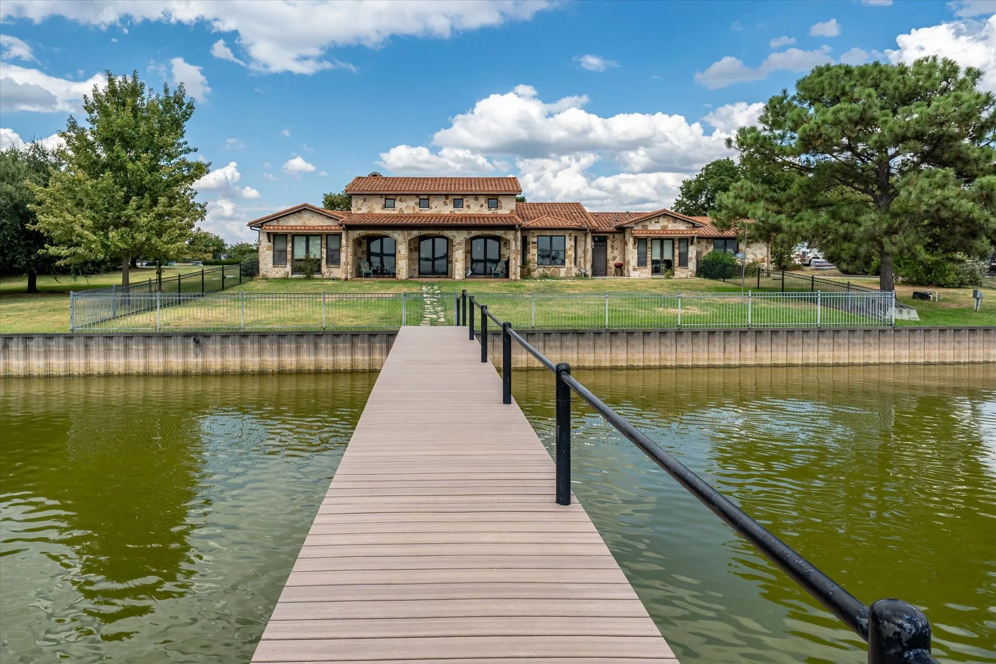 Waterfront property featuring a private dock, stone exterior, arched windows, and a tile roof
