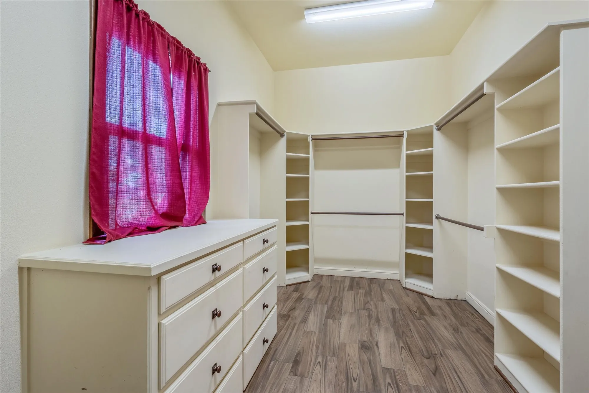 Walk-in closet featuring extensive built-in shelving, multiple hanging rods, integrated drawer storage, wood-finish flooring, and natural light from a window