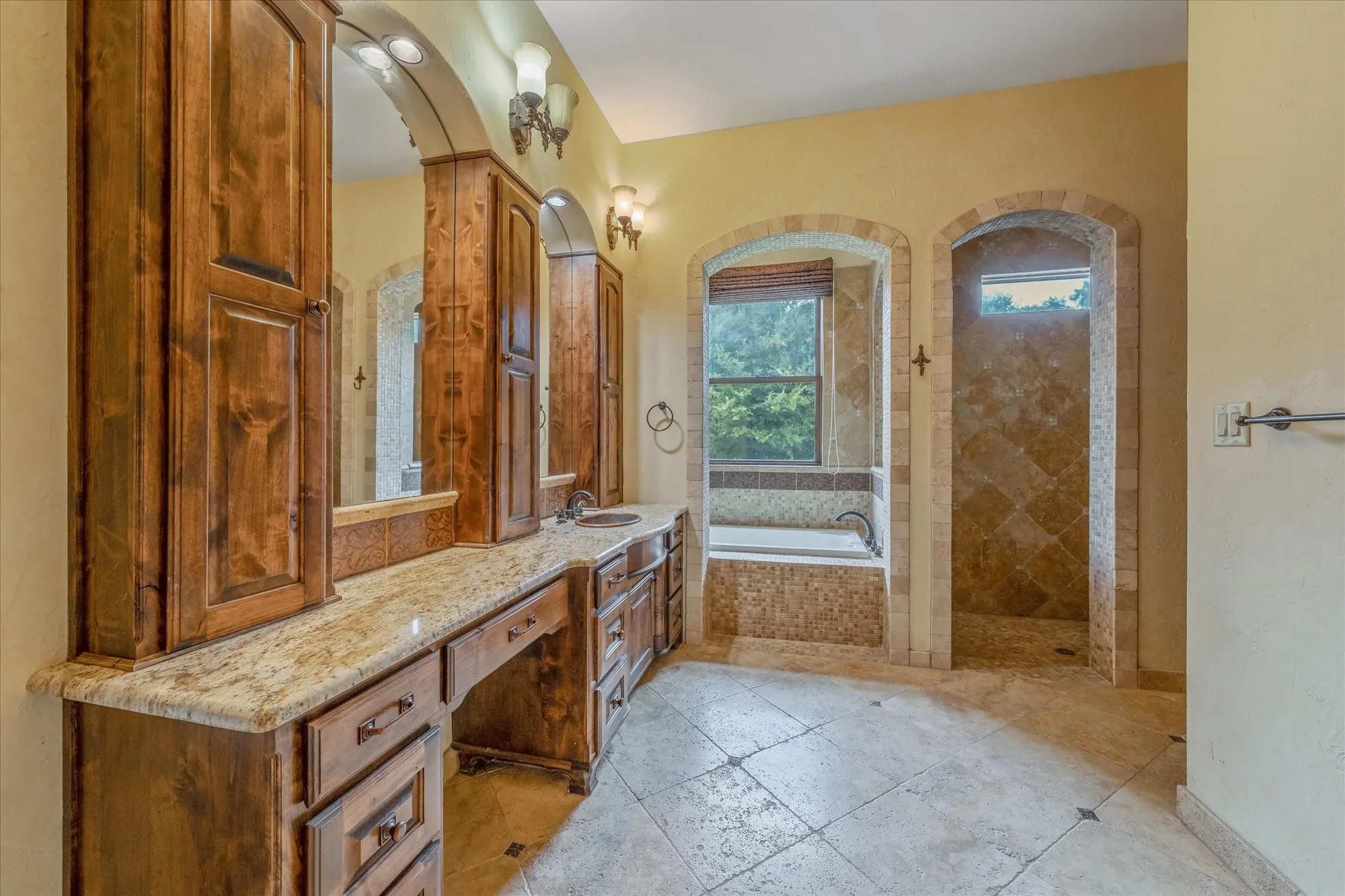 Dual wood-finish vanity with stone countertop, built-in storage, and arched mirrors