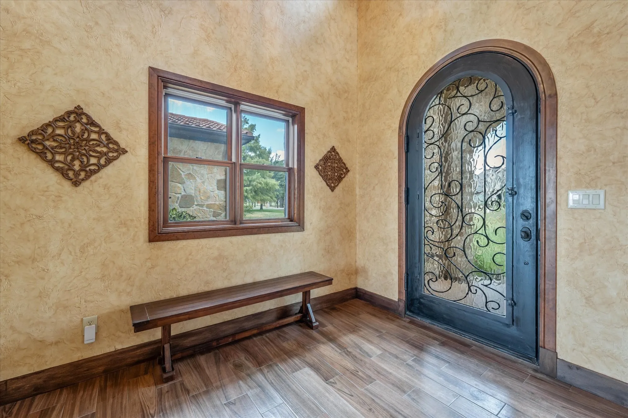 Arched entry door with decorative ironwork, wood-finish flooring, and textured wall finish