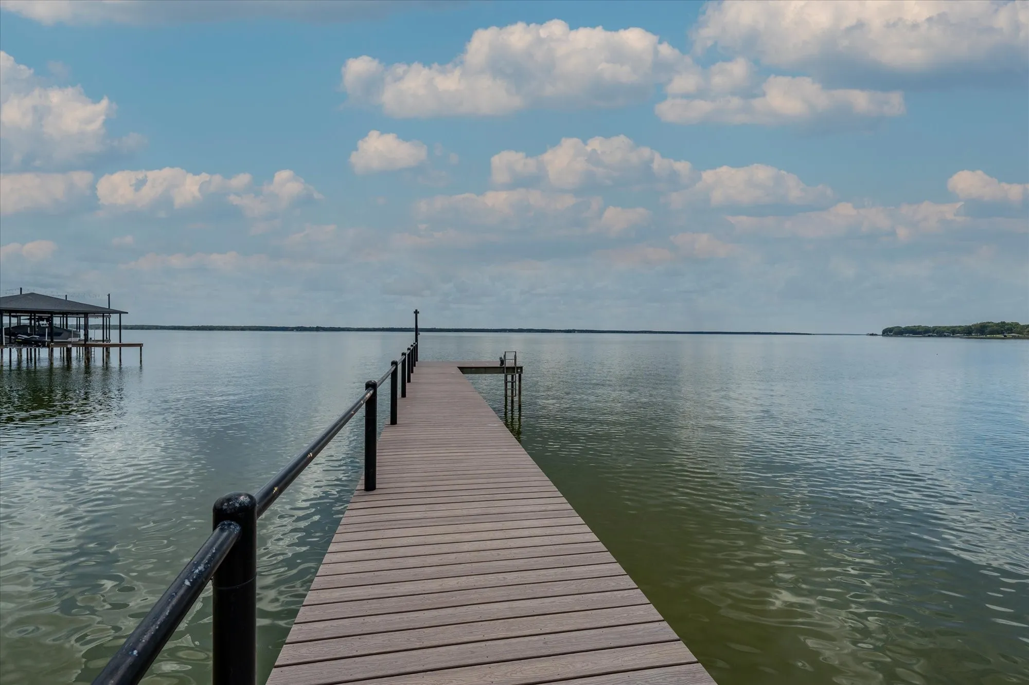 Waterfront property featuring a private dock with black railings, a boat lift, and a covered boat house