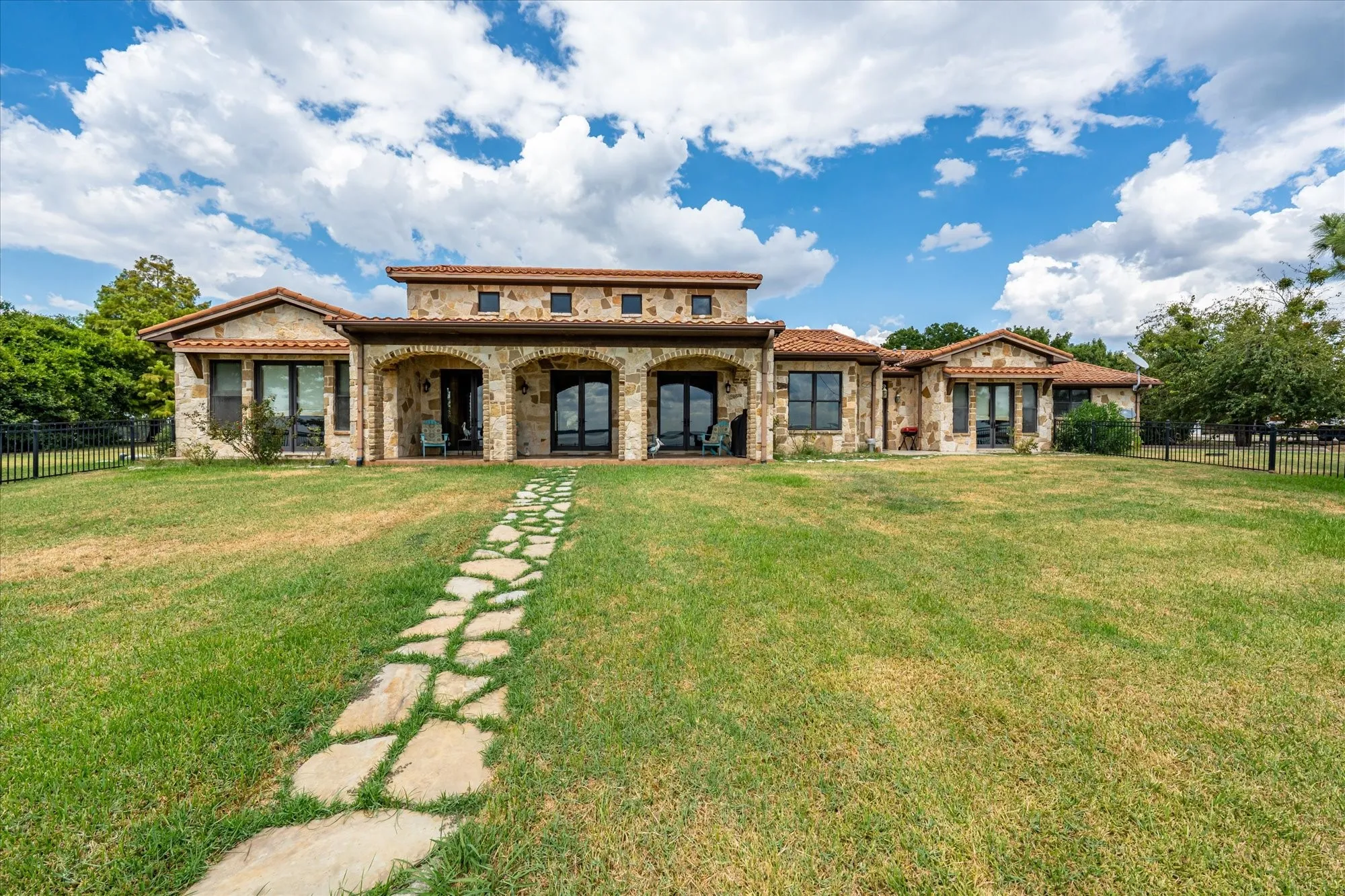 Stone facade residence featuring a tile roof, arched entryway, and multiple large windows