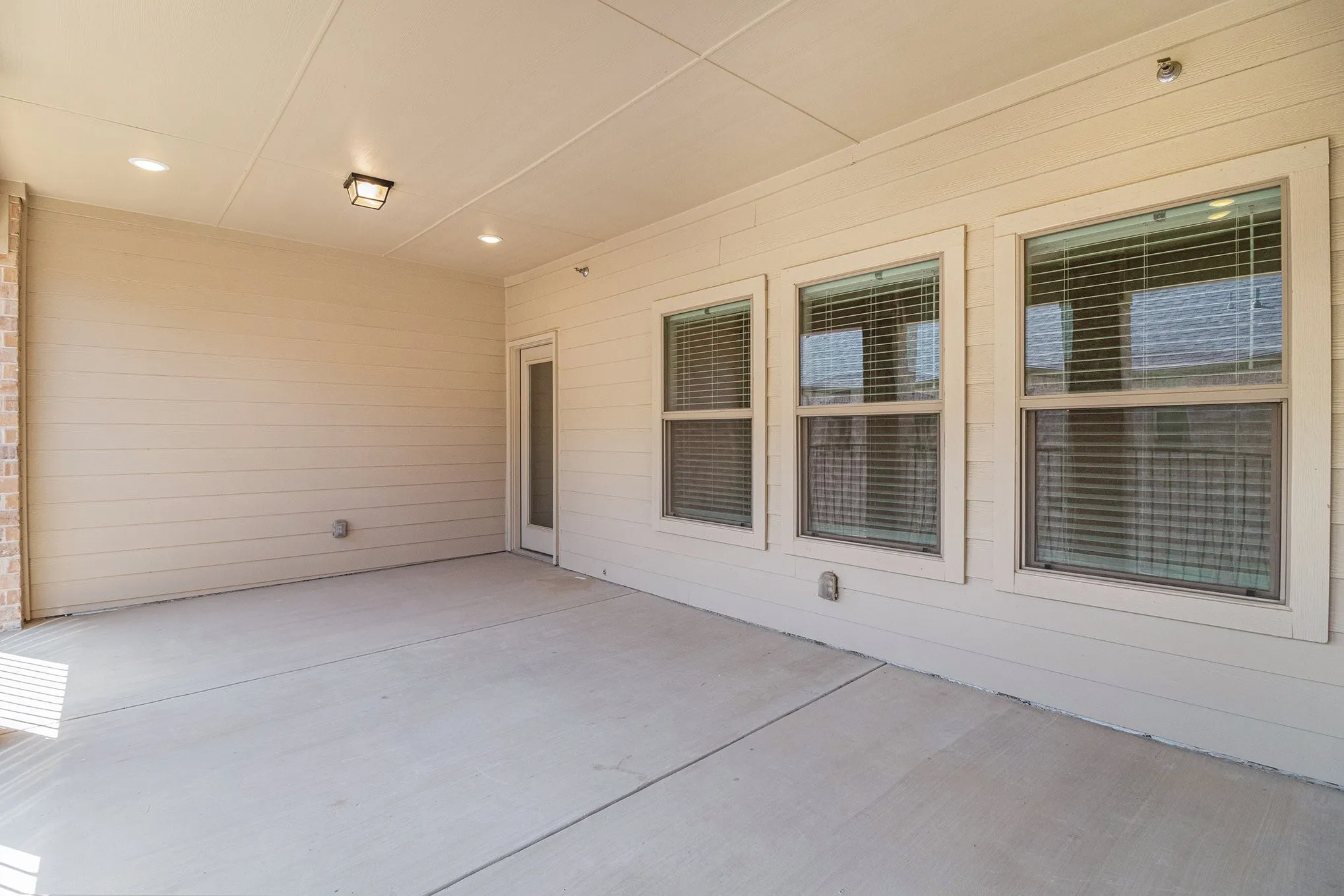 Covered concrete patio featuring recessed lighting, a ceiling-mounted fixture, three framed windows, and a glass-paneled door