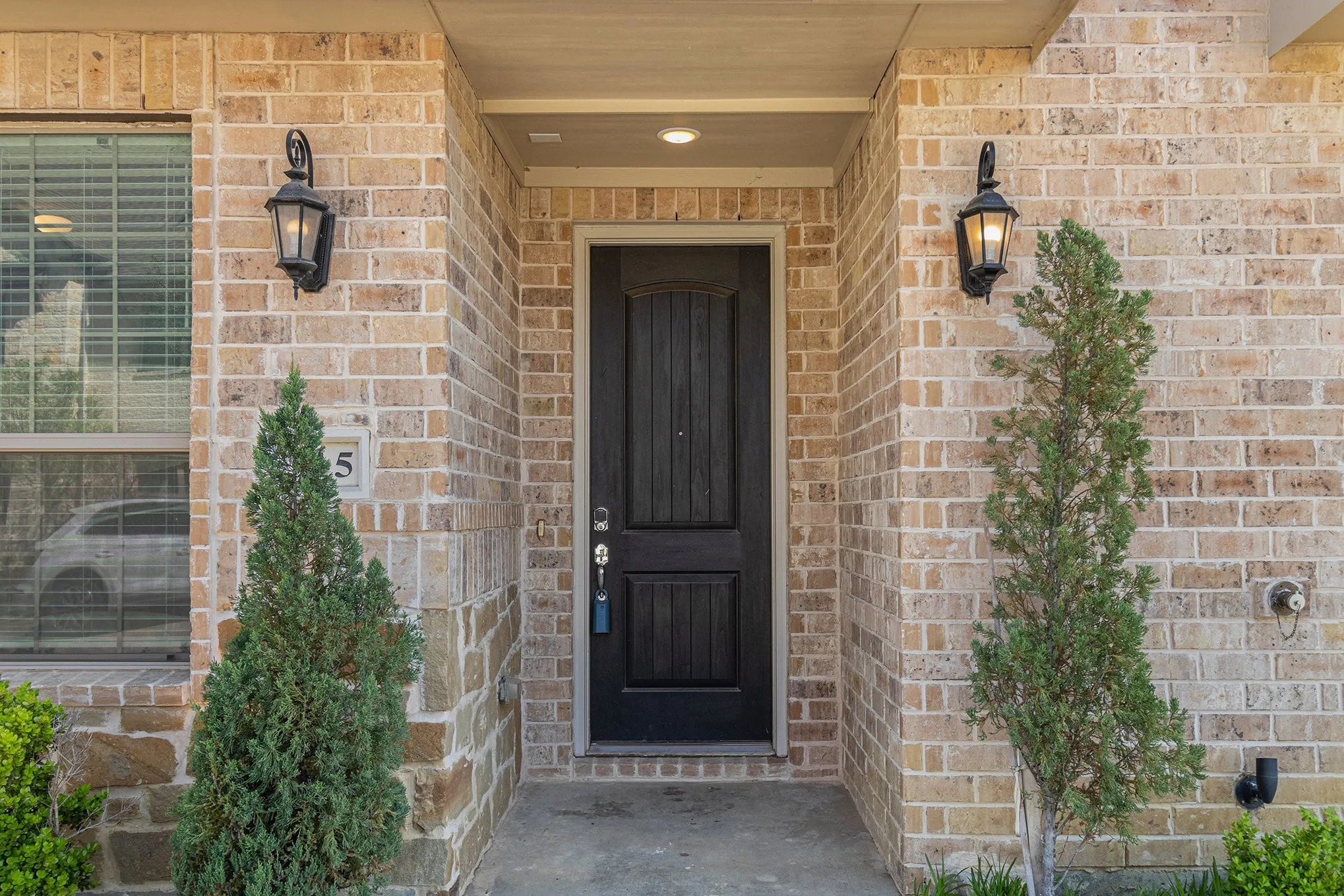 Brick exterior with a paneled entry door, two decorative exterior lanterns, and a covered entry