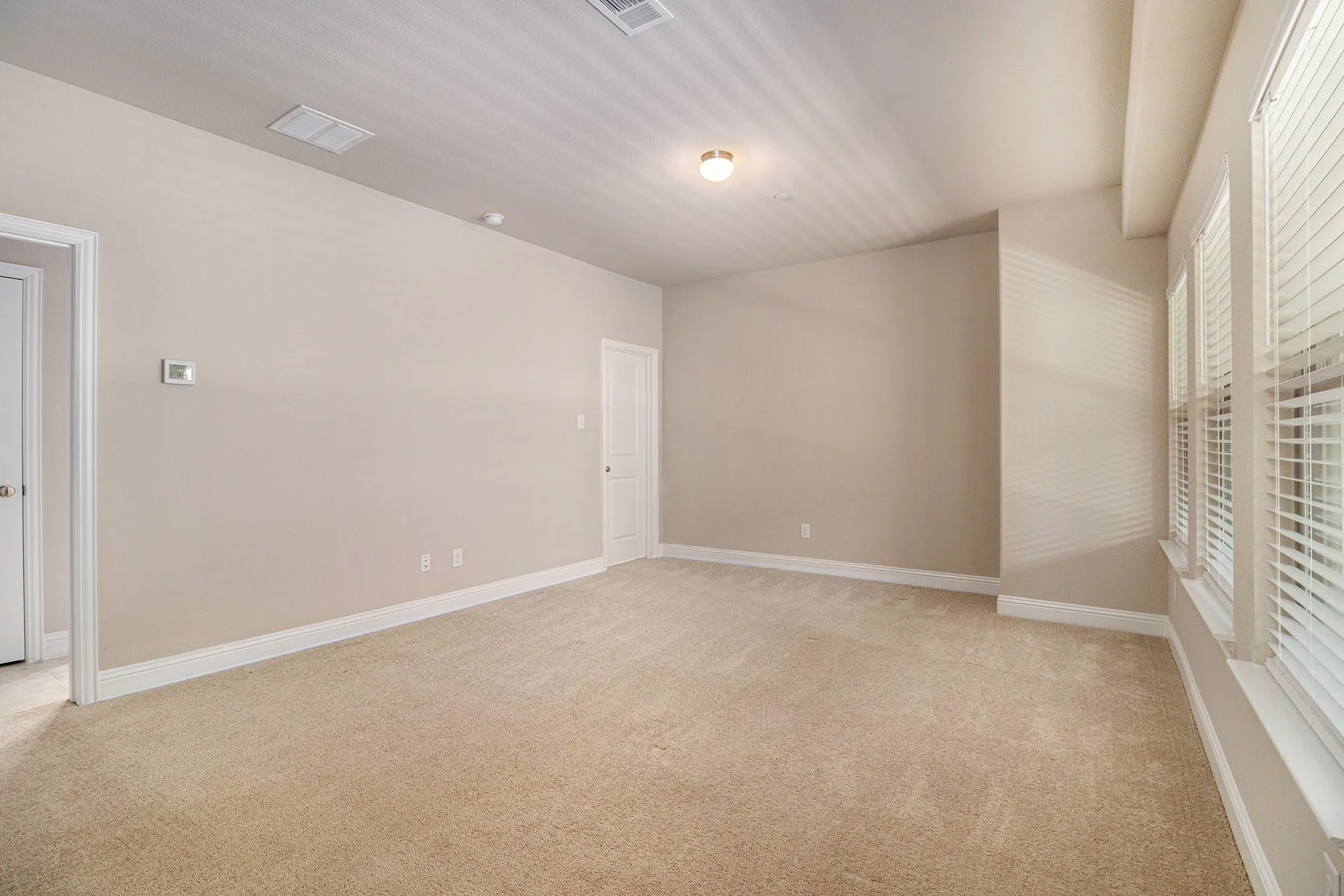 Neutral-toned walls, plush carpeting, multiple windows with blinds, recessed lighting, and a single ceiling-mounted light fixture