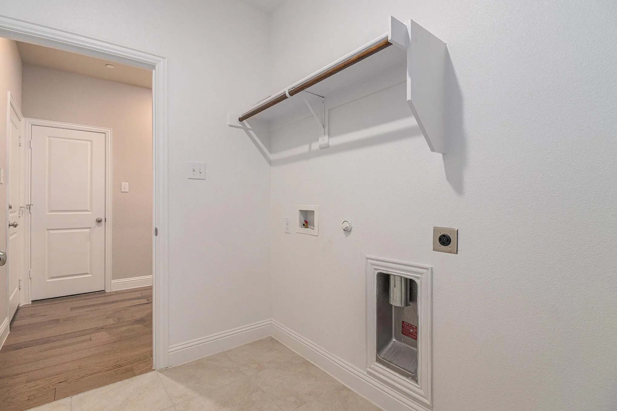 Laundry area with tile flooring, wall-mounted shelving, and wood-finish hanging rod