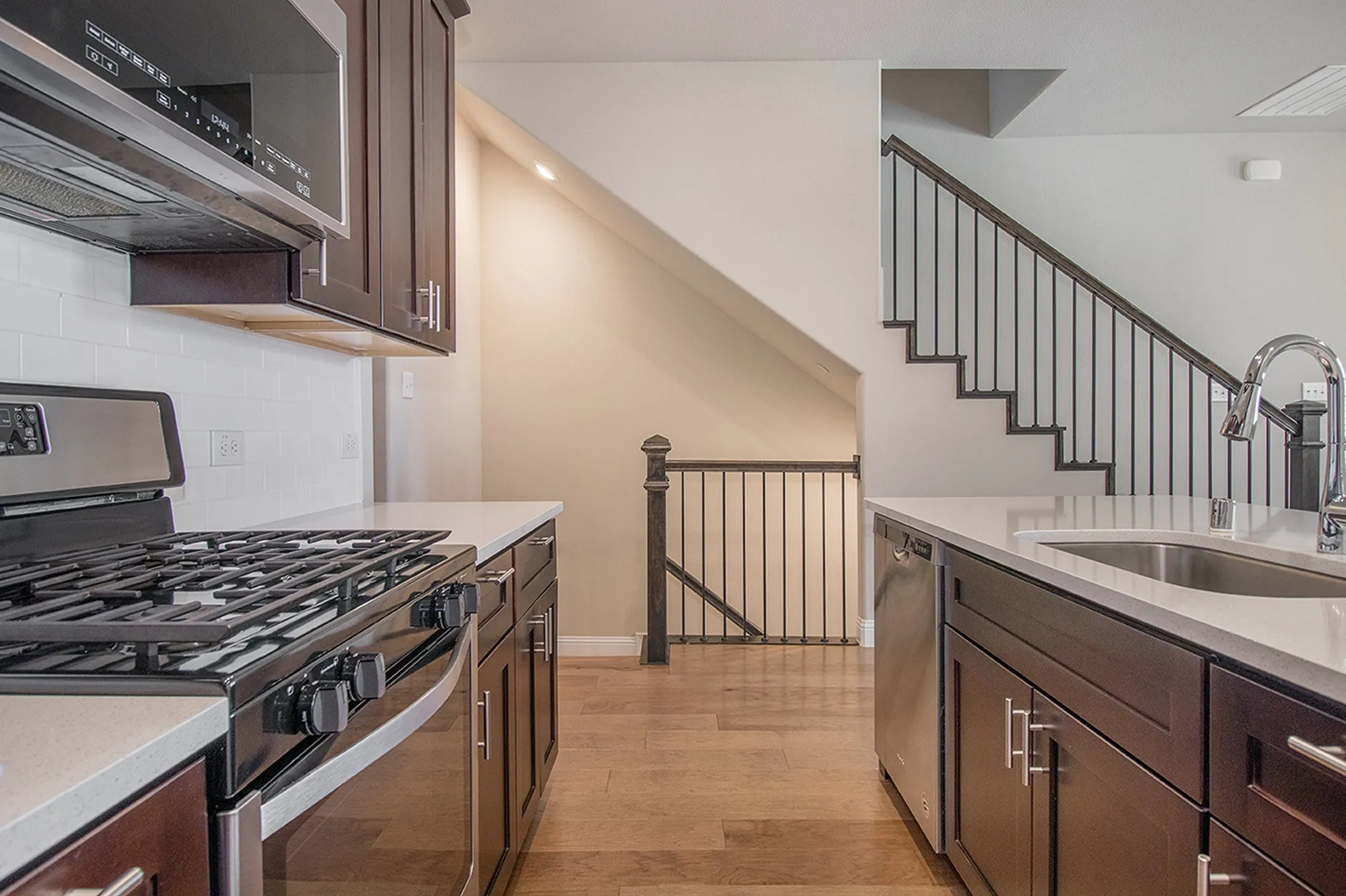Hardwood-finish flooring, dark wood cabinetry, white subway tile backsplash, stainless steel appliances, and white countertops