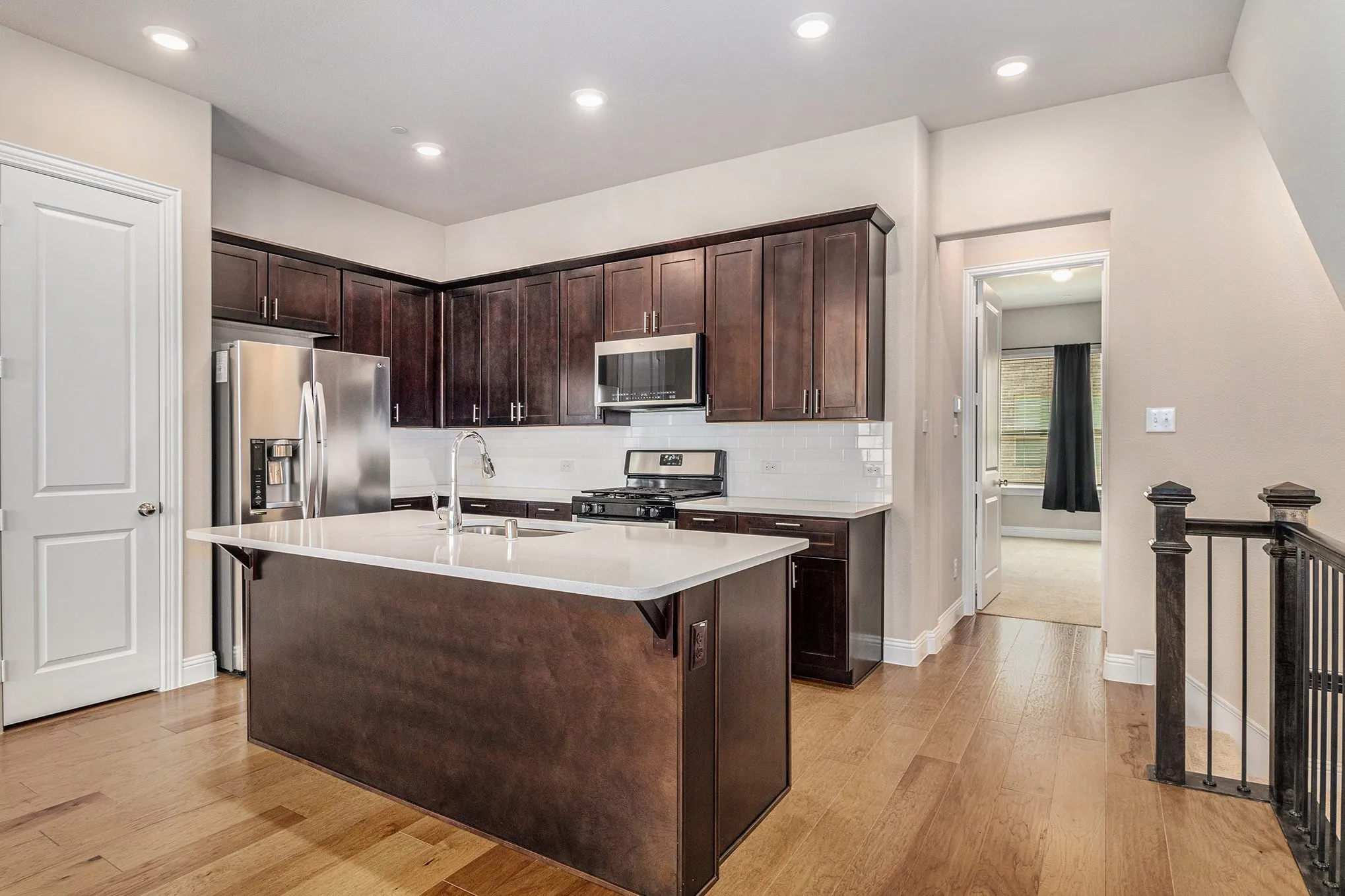 Kitchen featuring wood-finish flooring, dark wood cabinetry, white countertops, stainless steel appliances, and recessed lighting