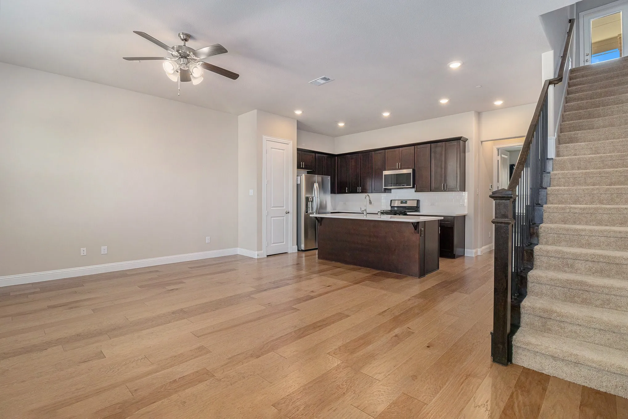 Wood-finish flooring, dark wood cabinetry, white kitchen island countertop, stainless steel appliances, and carpeted staircase