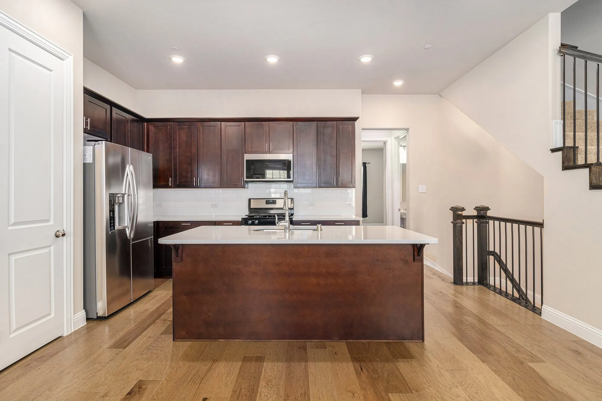 Kitchen featuring dark wood cabinetry, stainless steel appliances, a center island with a light-toned countertop, and wood-finish flooring