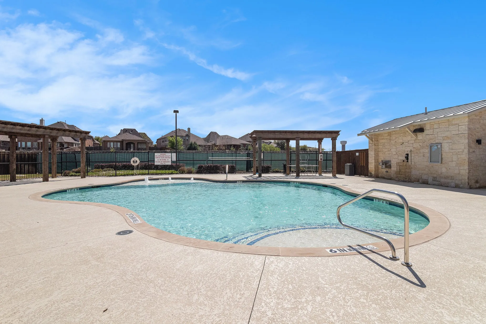 Freeform swimming pool with integrated spa and deck-mounted handrail, surrounded by a concrete deck