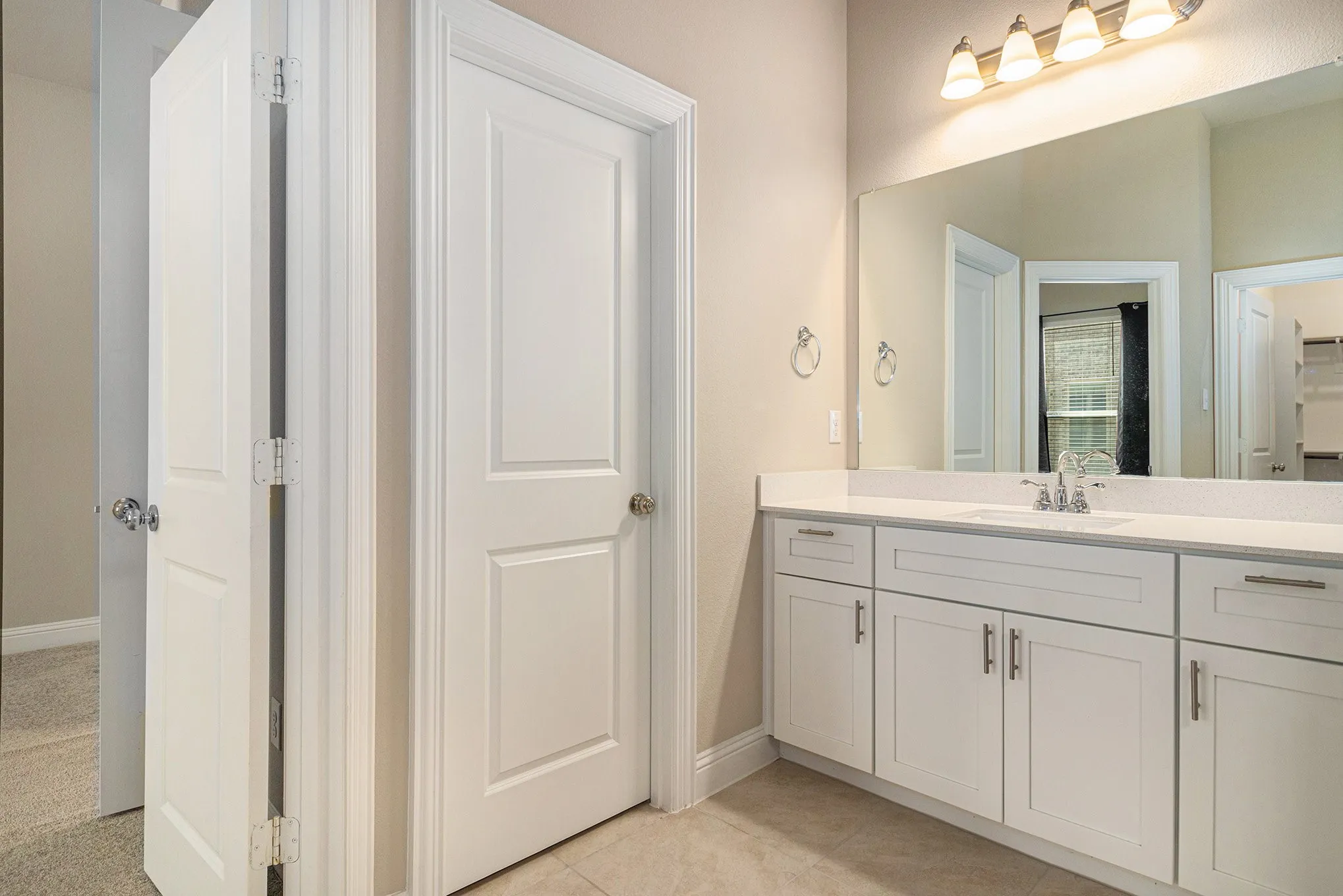 White vanity with integrated sink, stone countertop, brushed nickel faucet, large mirror, and overhead lighting