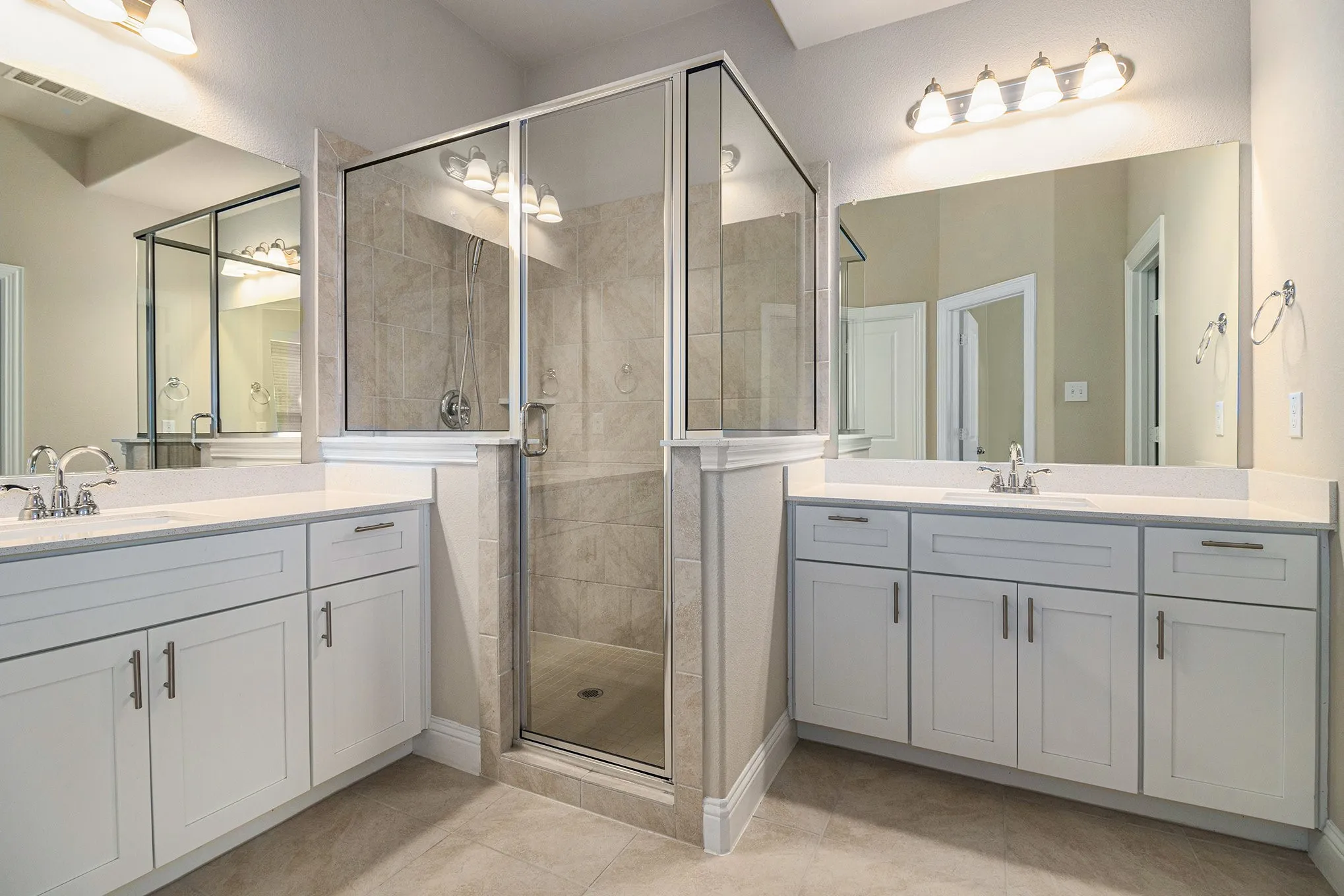 Dual vanity with light-toned cabinetry and integrated sinks, large mirrors, a glass-enclosed shower with tiled walls, and tile flooring