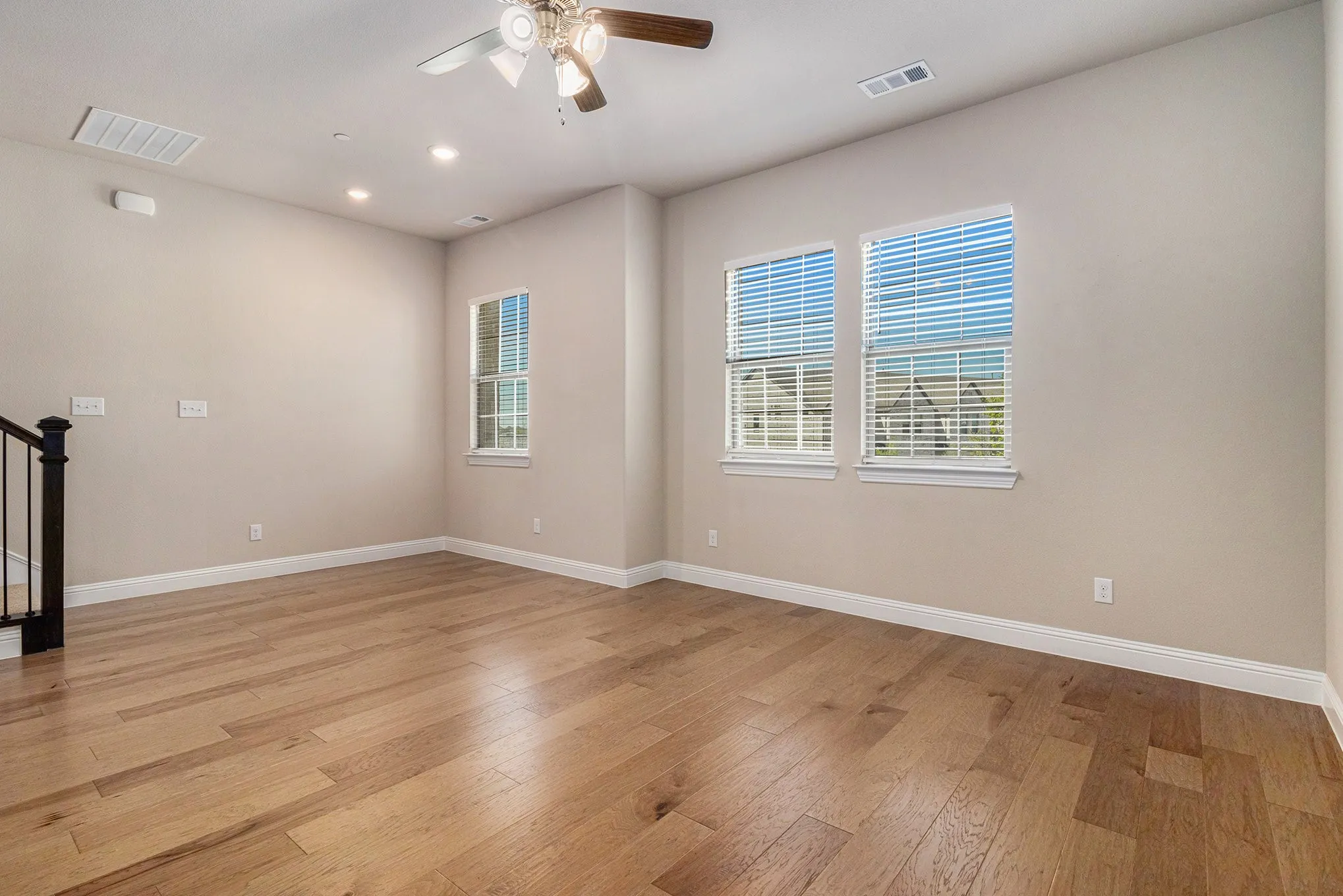 Hardwood flooring, recessed lighting, ceiling fan, white window blinds, and staircase with black iron balusters