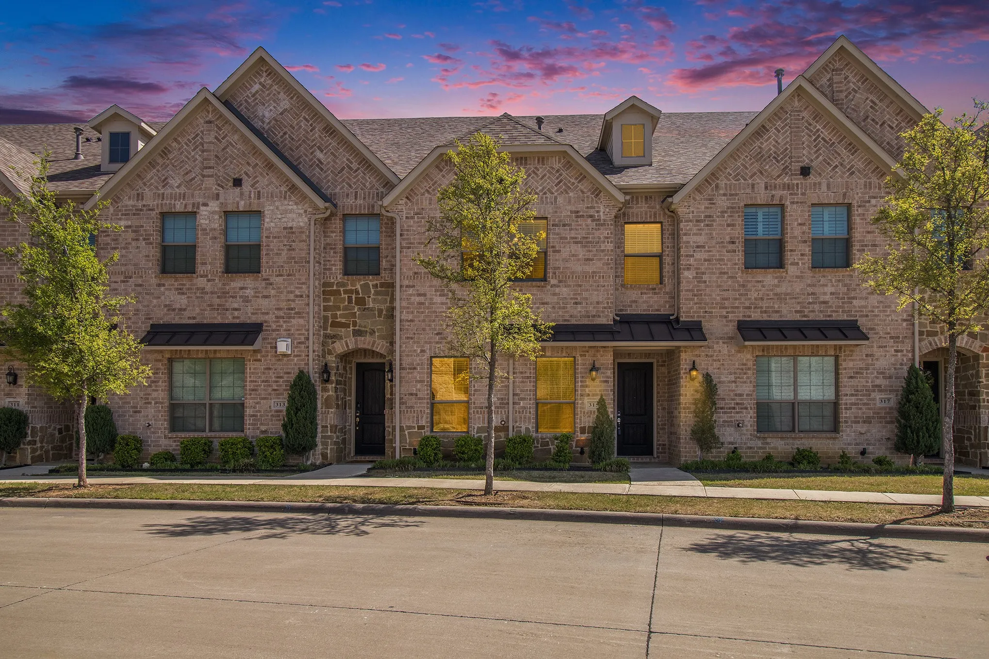 Brick and stone facade with gabled roof lines, featuring covered entryways, exterior lighting, and mature trees