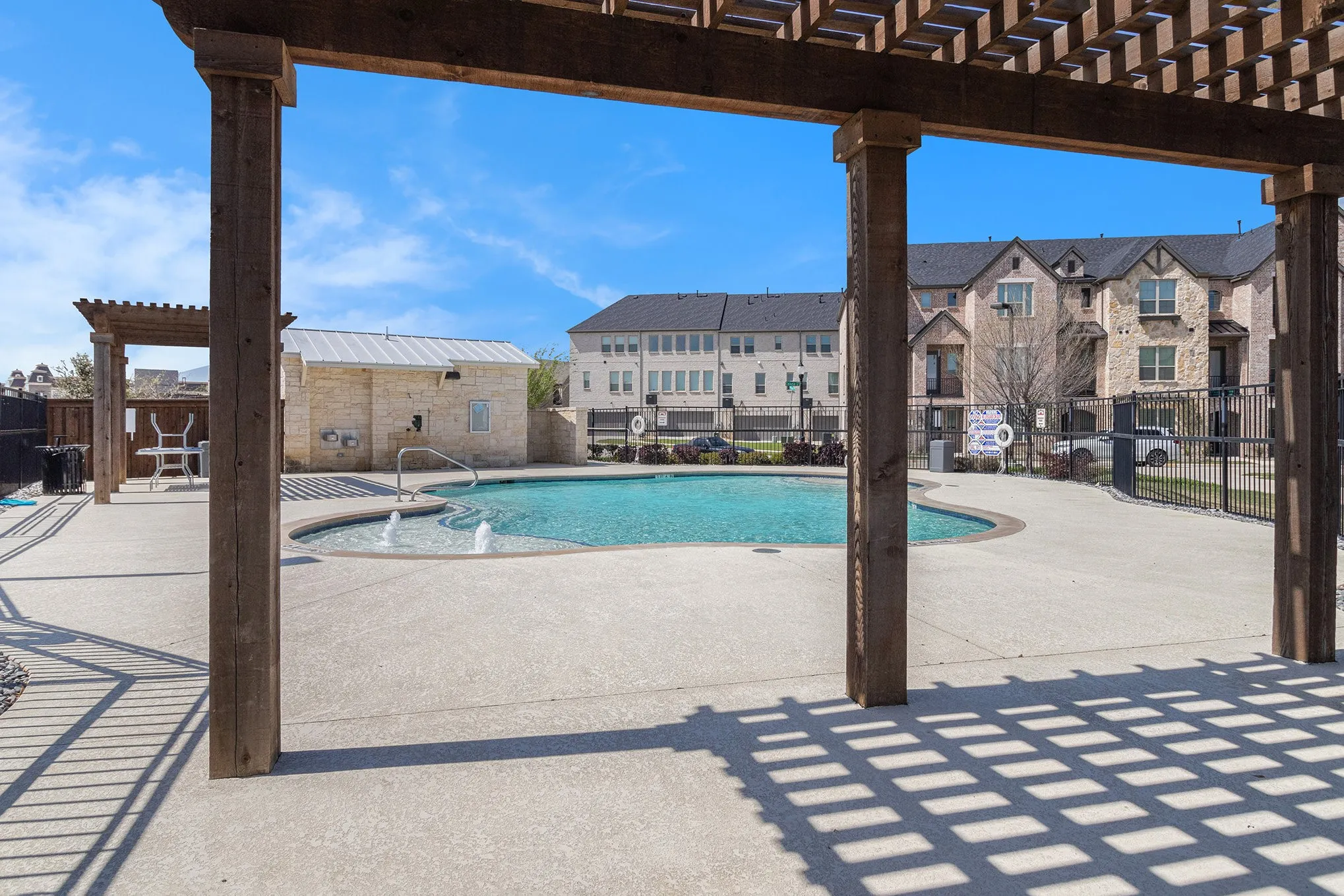 Swimming pool with integrated fountains, surrounded by concrete decking, stone-clad pool house, and multiple pergolas