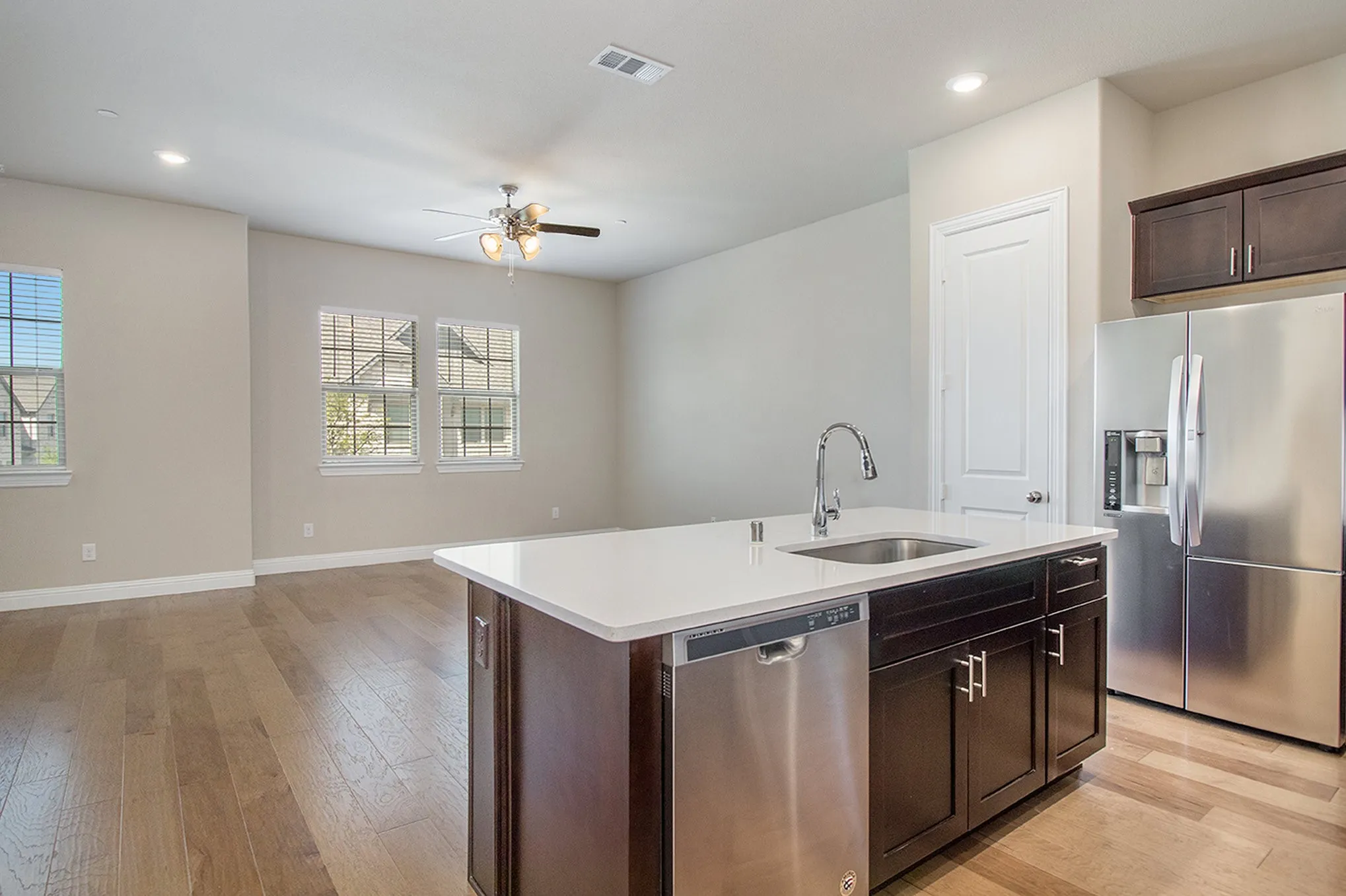 Kitchen island with an undermount sink, stainless steel appliances, dark wood-finish cabinetry, and light-tone countertops
