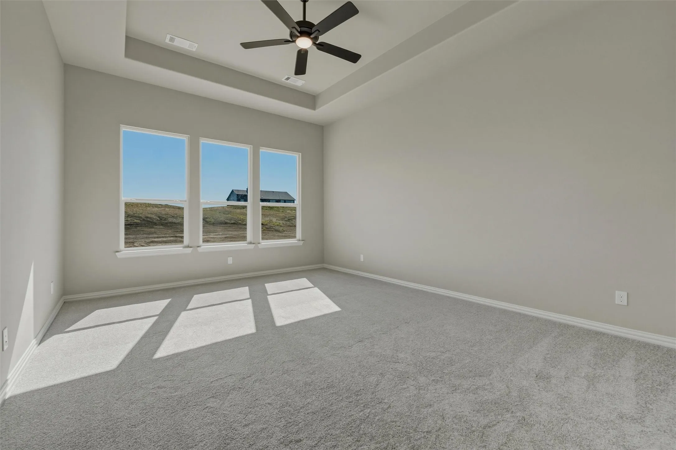 Tray ceiling with a ceiling fan, three pane windows, and gray carpeting