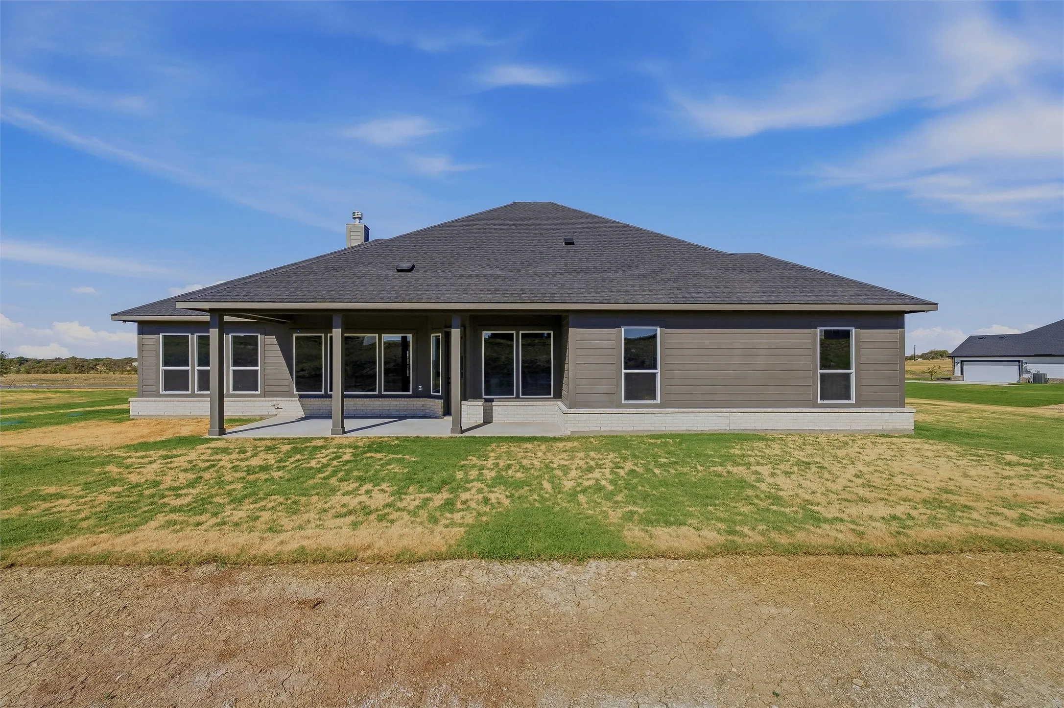Covered patio with concrete flooring, dark gray siding, multiple windows, and a dark shingle roof