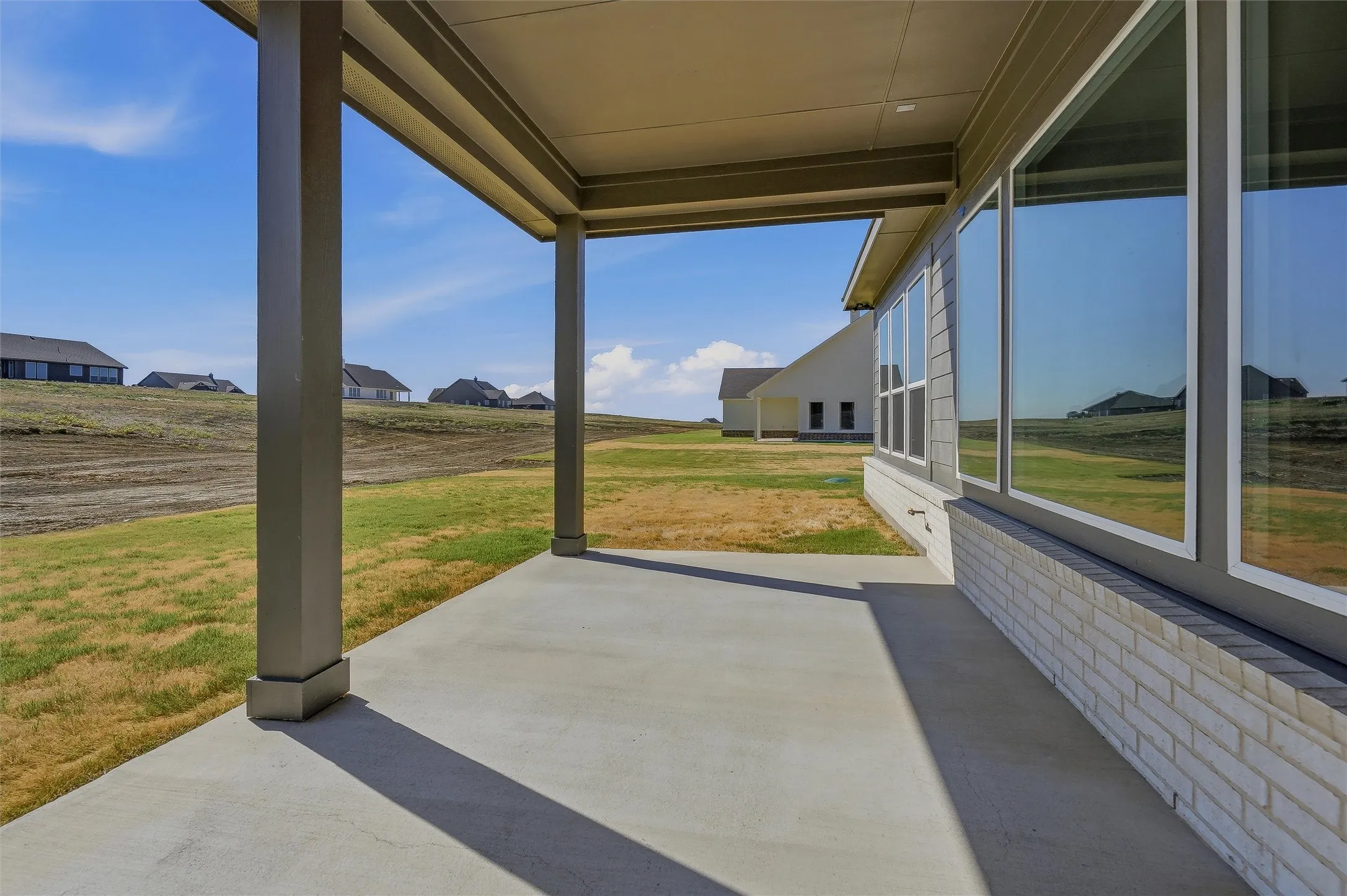 Covered patio with concrete flooring, multiple large windows, and a white brick foundation