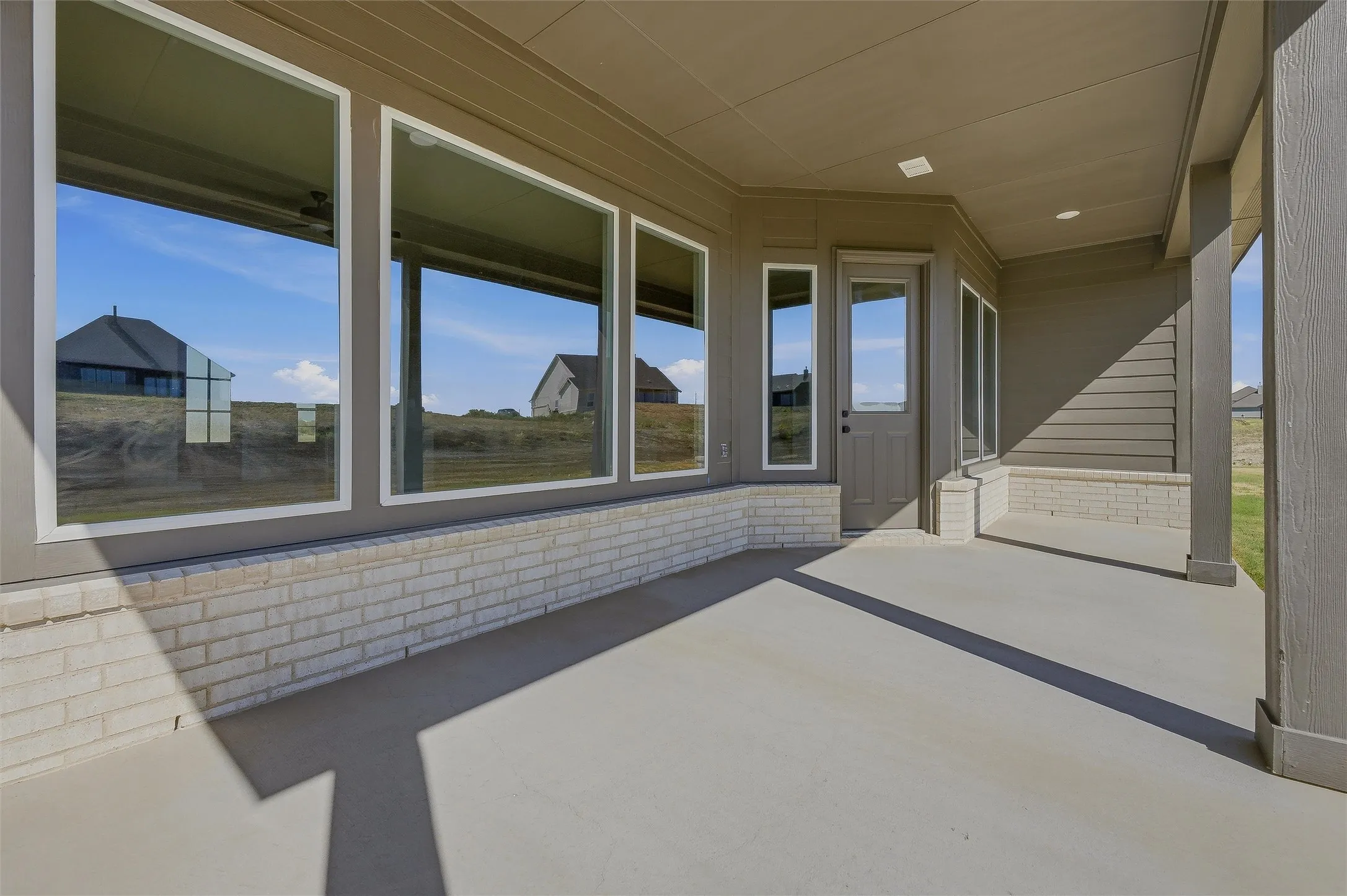 Expansive covered patio with a concrete surface, white brick accents, and multiple large windows