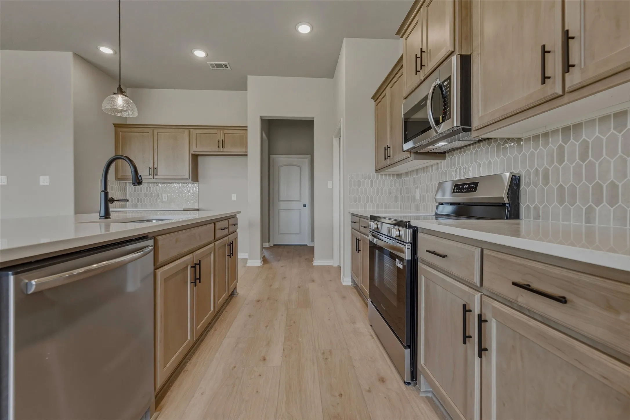 Kitchen featuring wood-finish flooring, light-toned cabinetry, stainless steel appliances, a tile backsplash, and a central island with a sink