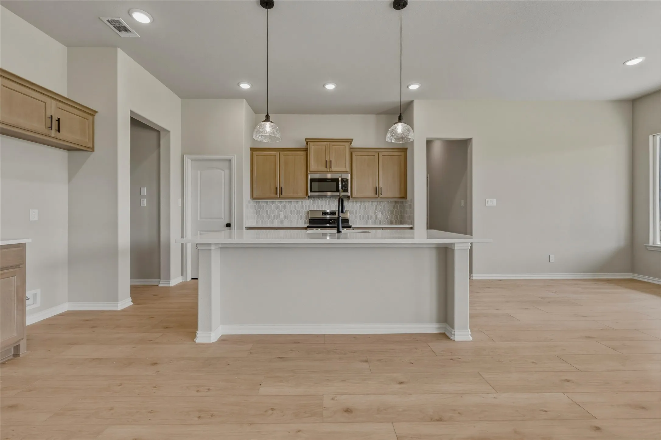 Kitchen featuring a large island with white countertop, pendant lighting, wood-finish flooring, light-toned cabinetry, and recessed lighting