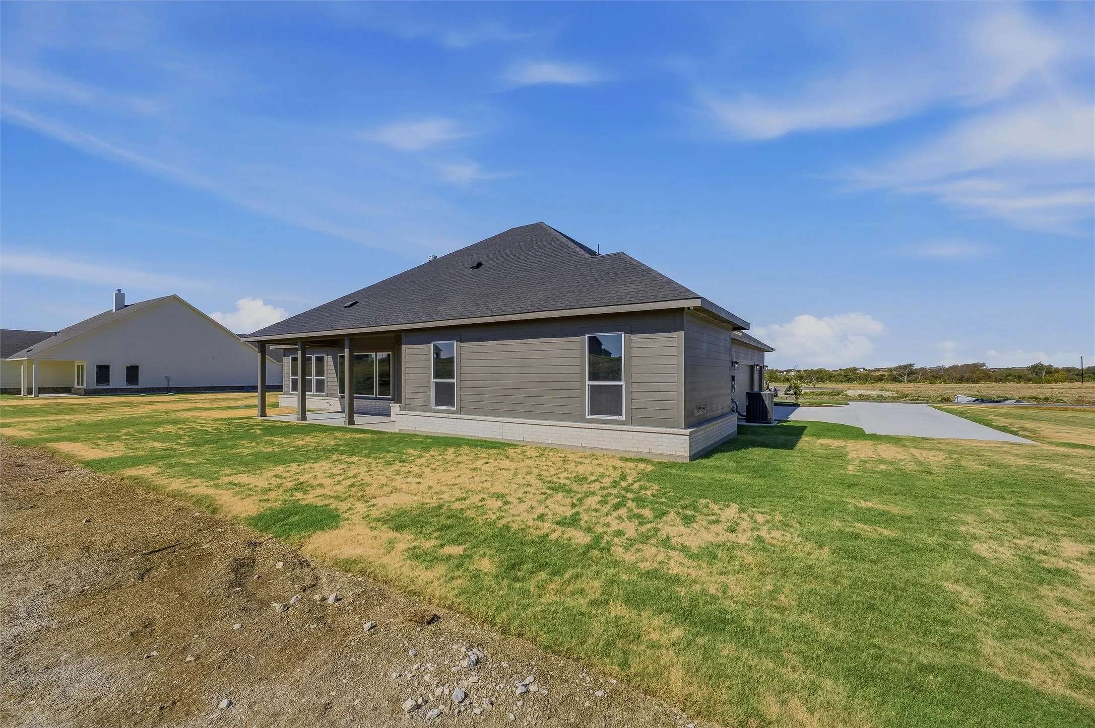 Siding exterior with a covered patio, dark shingle roof, and concrete foundation