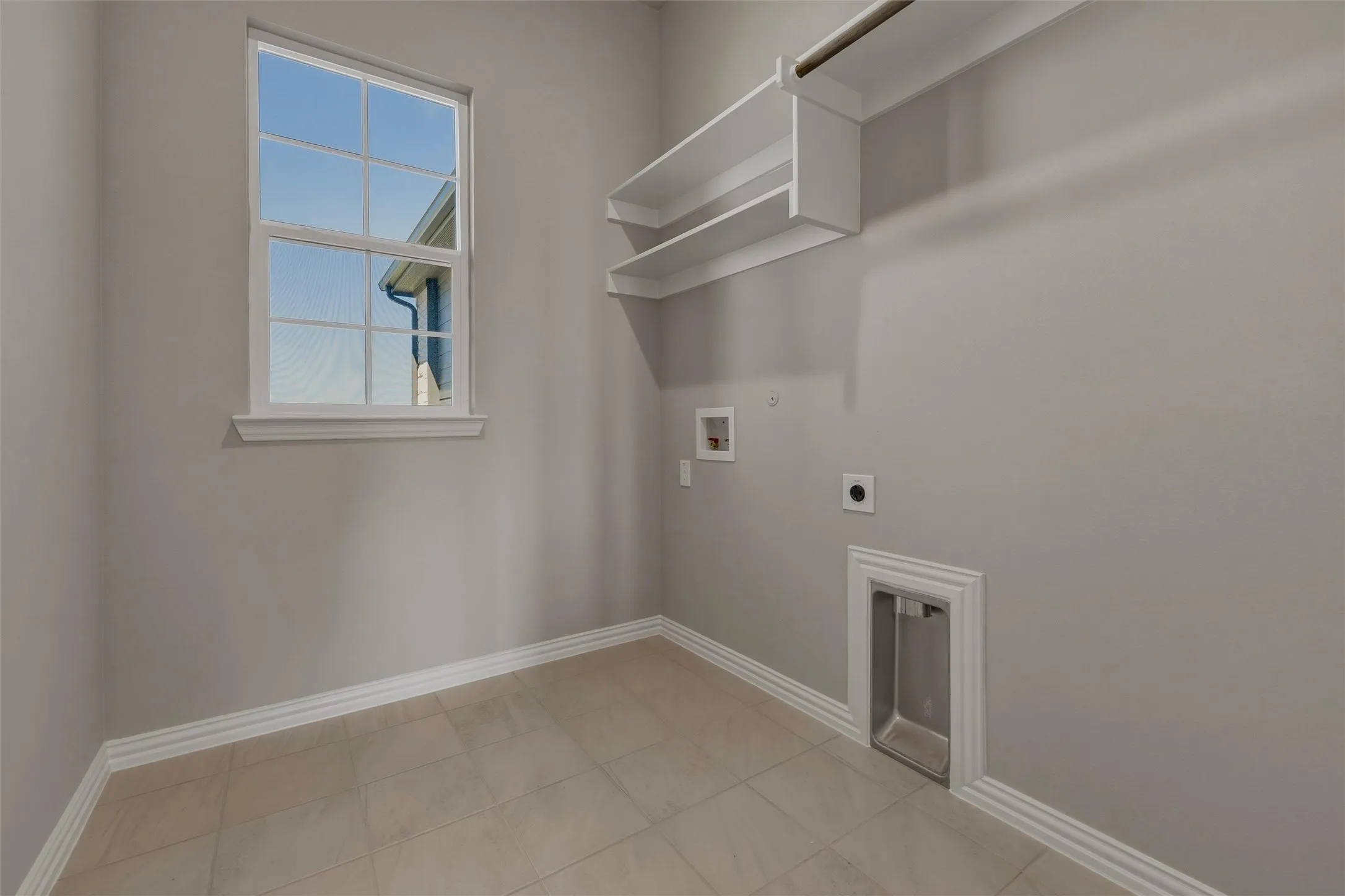 Tile flooring, built-in shelving, clothes hanging rod, window, and wall-mounted utility connections