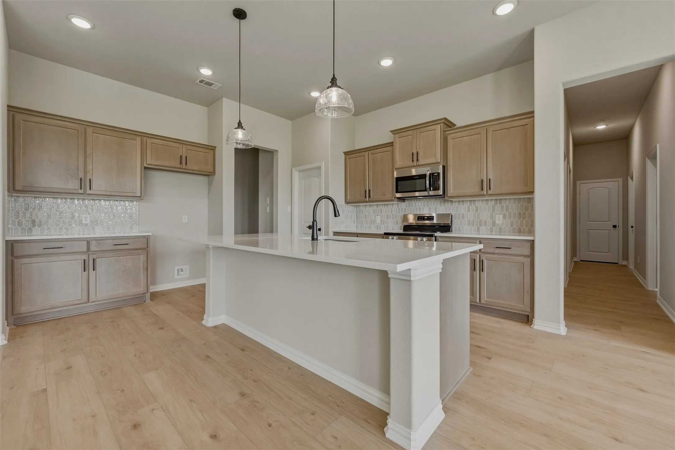 Spacious kitchen featuring light wood-finish flooring, a kitchen island with a white countertop and integrated sink, stainless steel appliances, and light-toned cabinetry