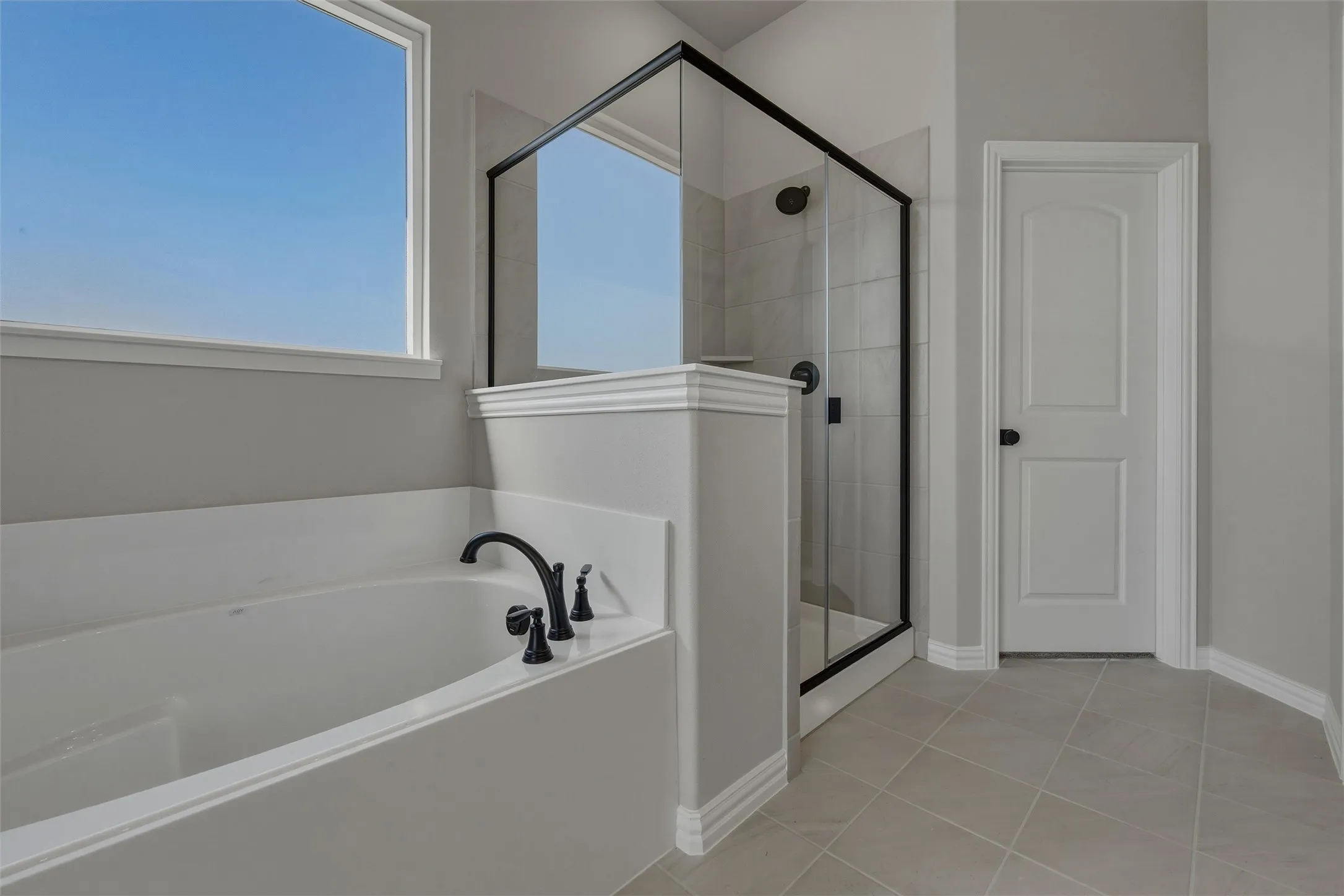 Built-in soaking tub with matte black fixtures, separate glass-enclosed shower with matte black fixtures, tiled flooring, and a window