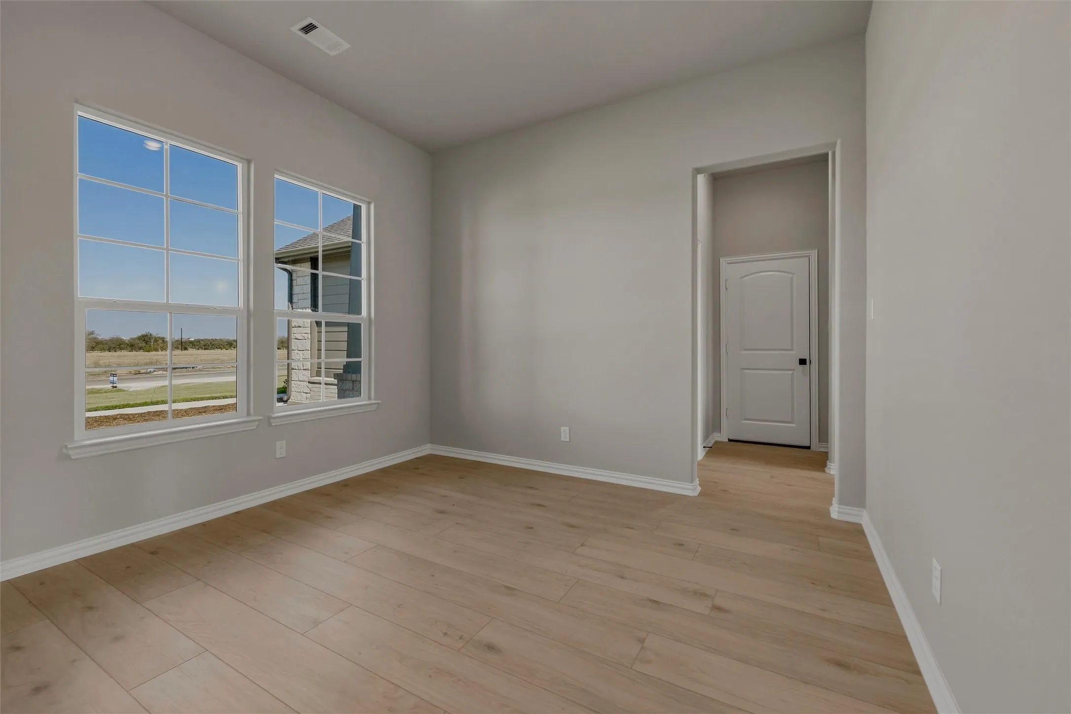 Light wood-finish flooring, neutral wall tones, white trim, and a paneled interior door with matte black hardware