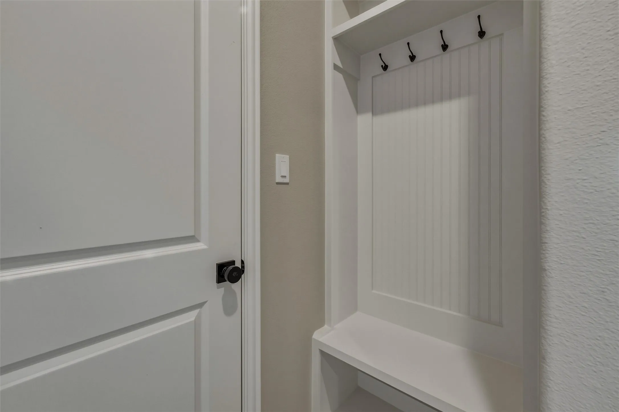 Built-in storage unit with beadboard backing and black hooks, complemented by a white paneled door with a black knob