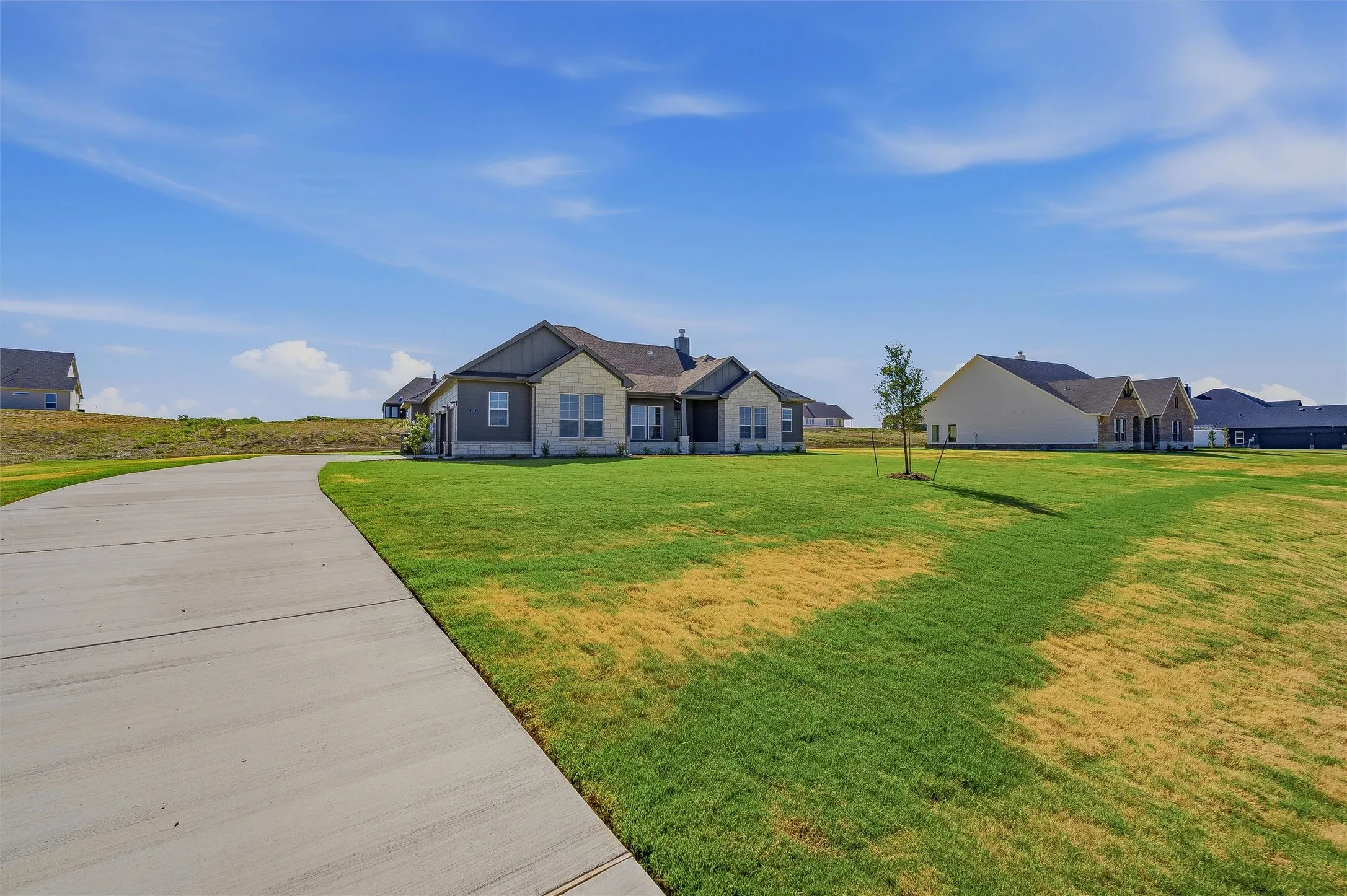 Exterior featuring stone and siding finishes, a gabled roof, and an expansive concrete driveway