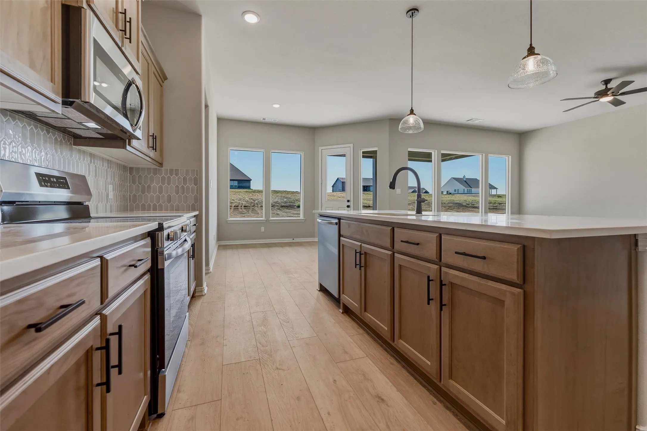 Kitchen featuring a central island with an undermount sink, pendant lighting, wood-finish flooring, stainless steel appliances, and light-toned cabinetry