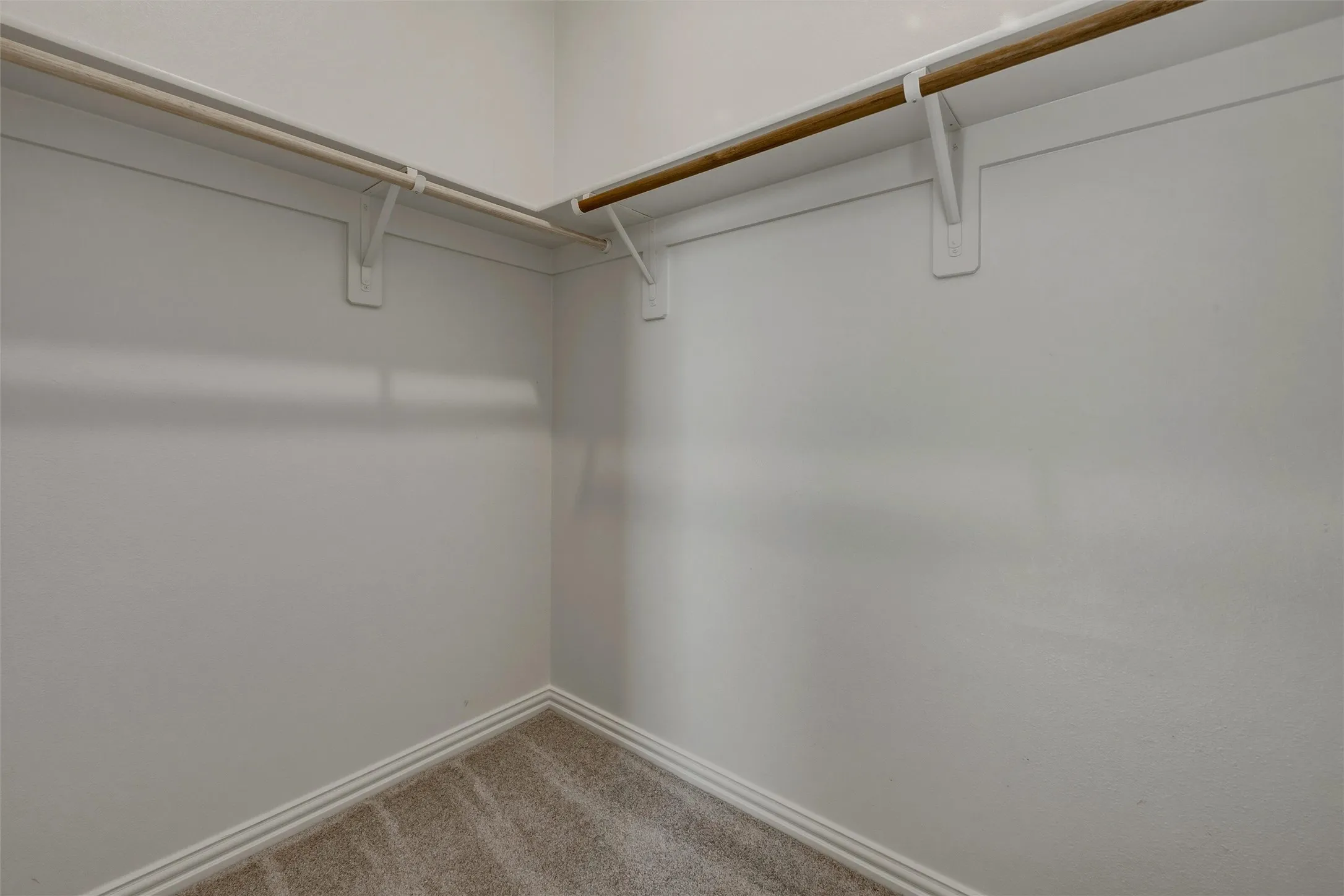 Carpeted flooring with baseboard trim, and two installed clothing rods