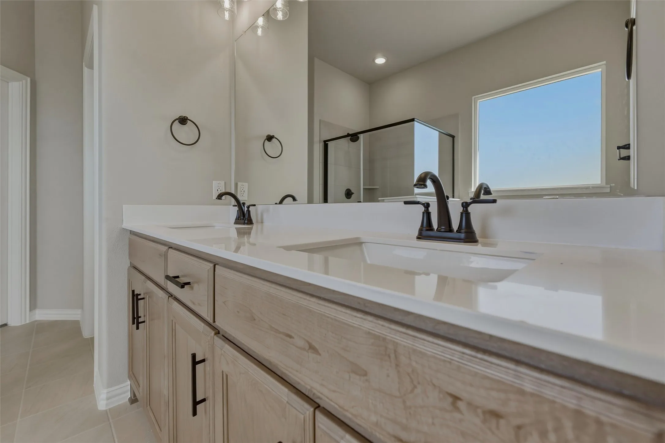 Dual vanity with light wood-finish cabinetry, white countertops, and matte black fixtures