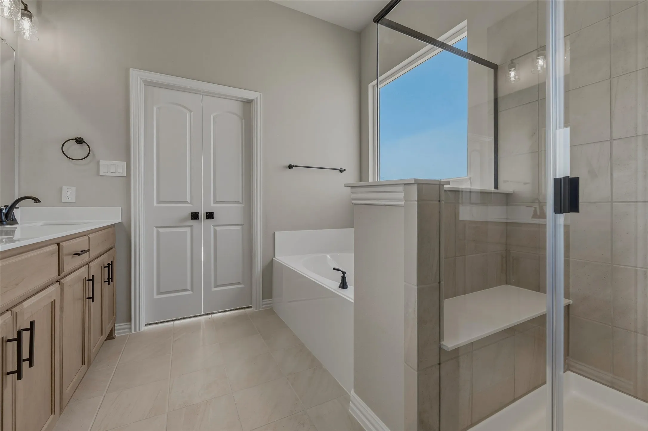 Dual wood-finish vanity with countertop, glass-enclosed shower with tiled walls and built-in bench, freestanding bathtub, and tiled flooring