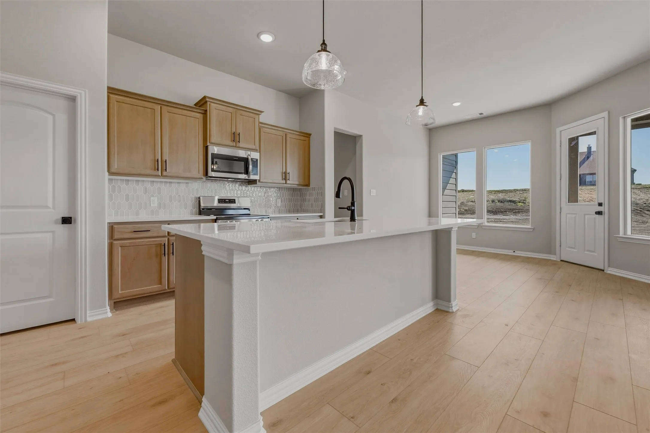 Kitchen featuring wood-finish cabinetry, stainless steel appliances, a white tile backsplash, and a large island with a composite countertop