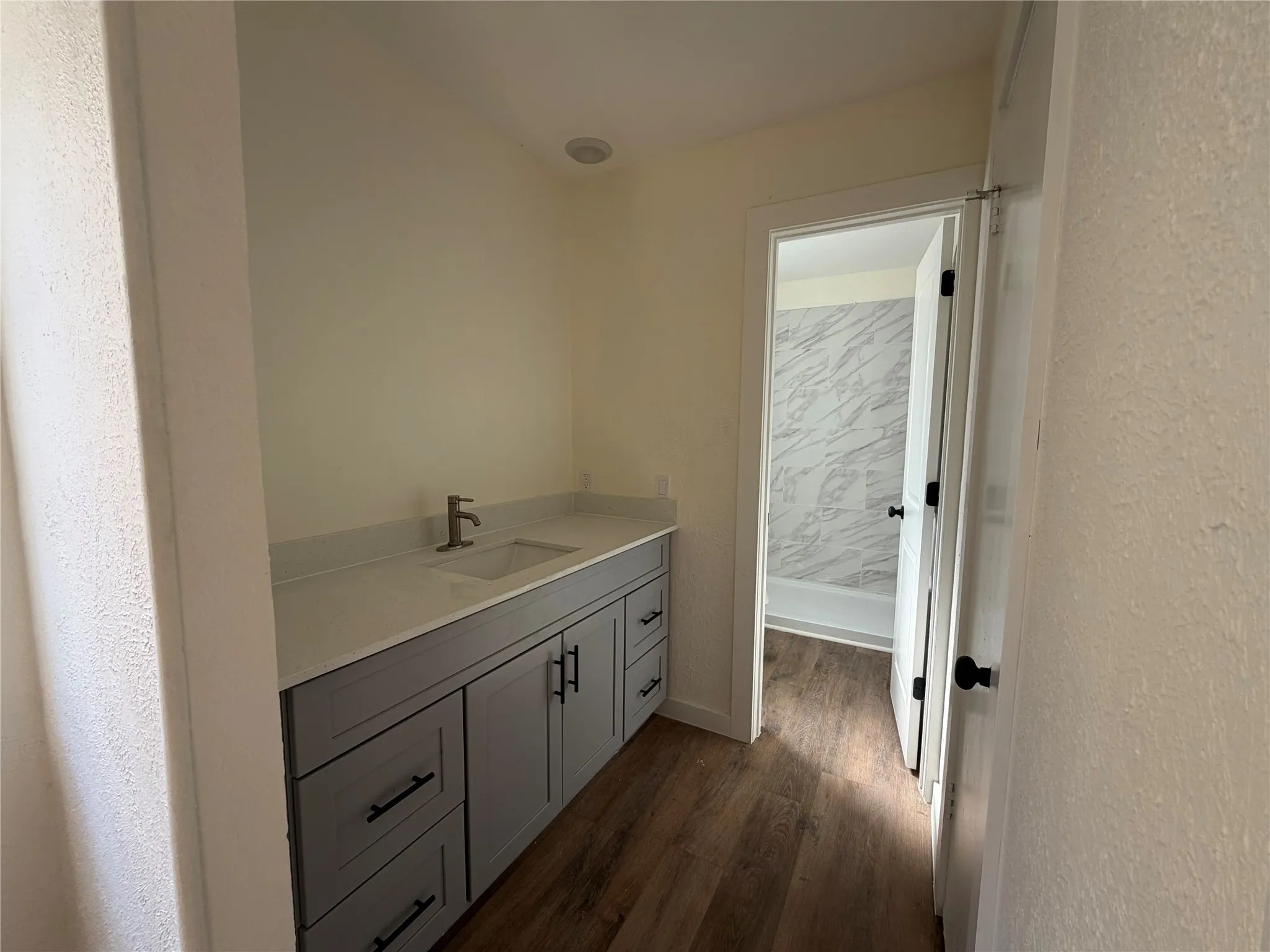 Recessed lighting, gray cabinetry with dark hardware, integrated sink, light-toned countertop, and wood-finish flooring