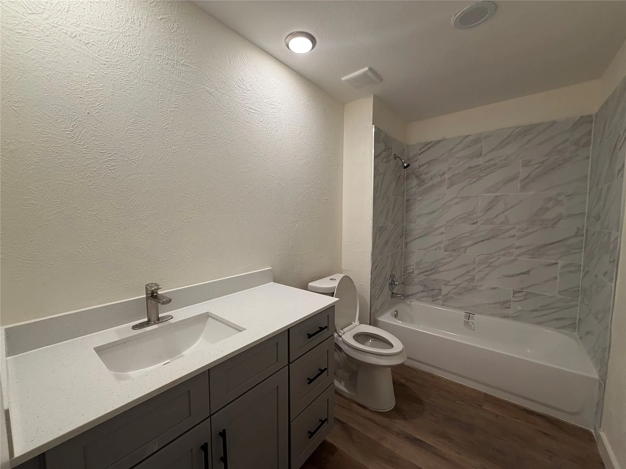 Bathroom featuring a single vanity with a white countertop, wood-finish flooring, and a bathtub with tiled walls
