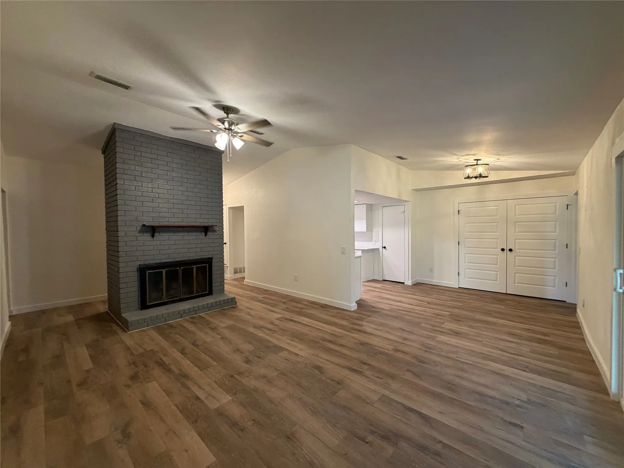 Spacious living area featuring wood-finish flooring, a painted brick fireplace, a ceiling fan, and a built-in light fixture