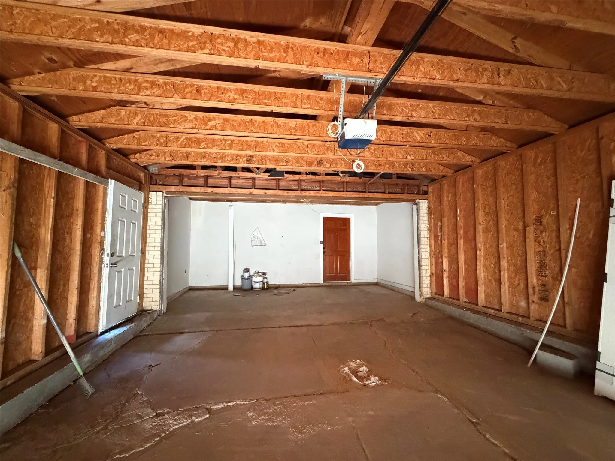 Unfinished garage interior with exposed wood framing, a concrete floor, and an automatic garage door opener