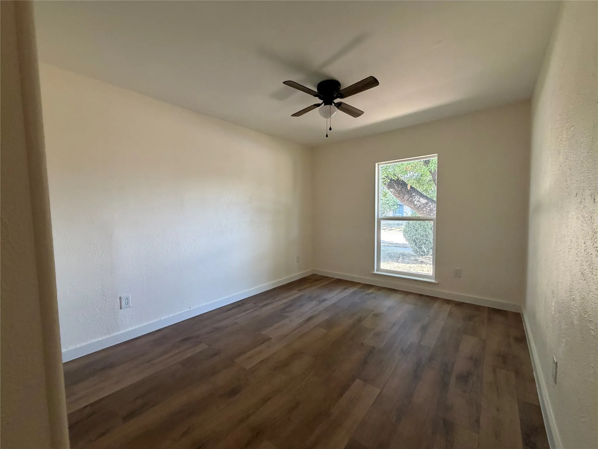Wood-finish flooring, single window, ceiling fan with light fixture, and neutral wall tones