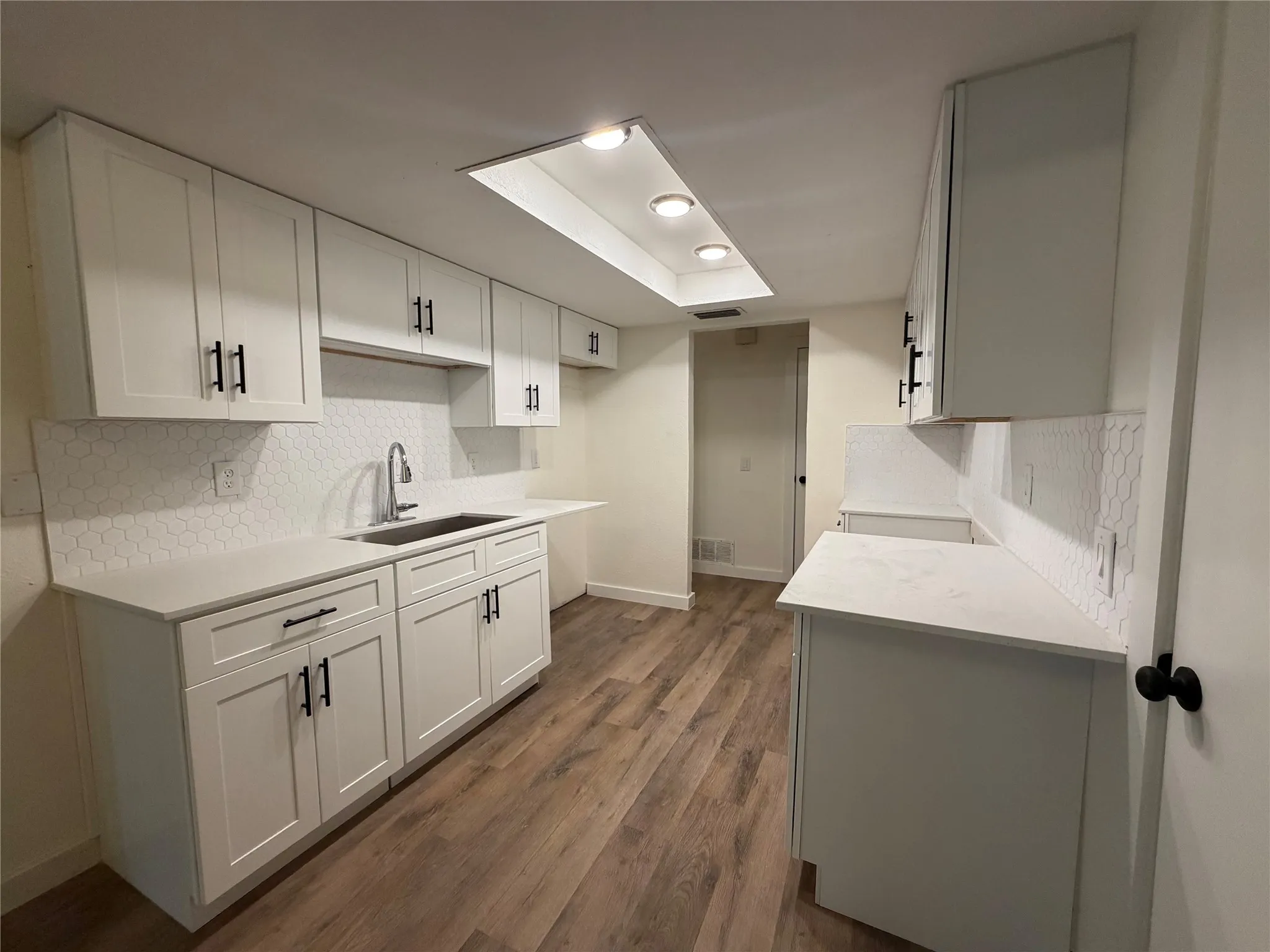 White shaker-style cabinetry with matte black hardware, white countertops, hexagon tile backsplash, wood-finish flooring, and recessed lighting