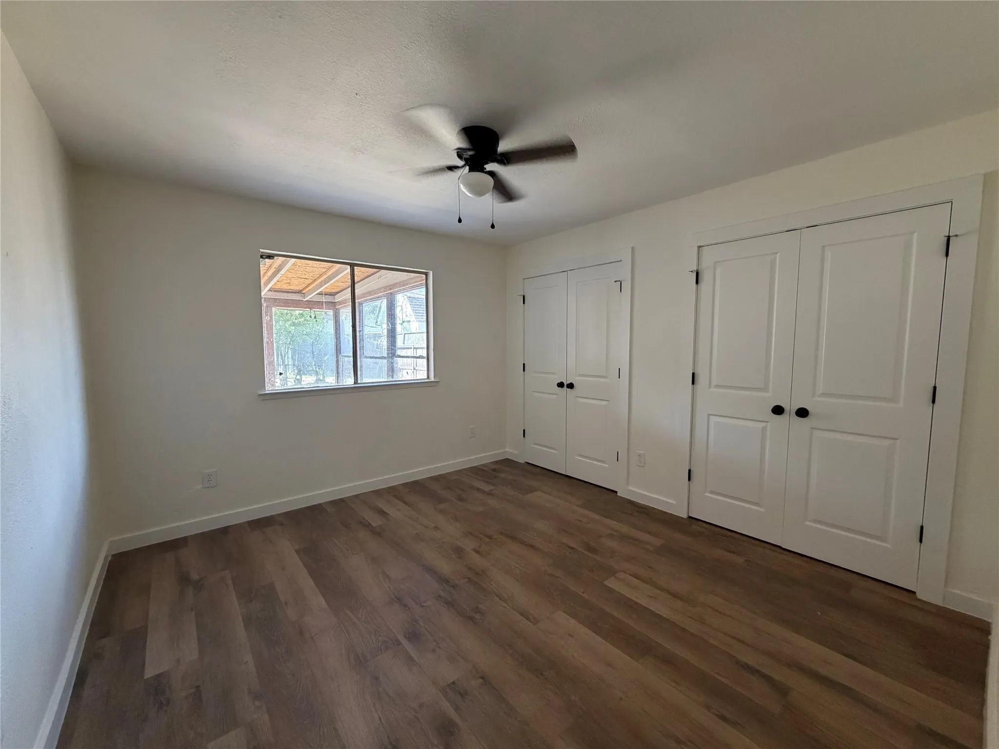 Wood-finish flooring, dual panel doors, a ceiling fan, and a window with exterior screen enclosure