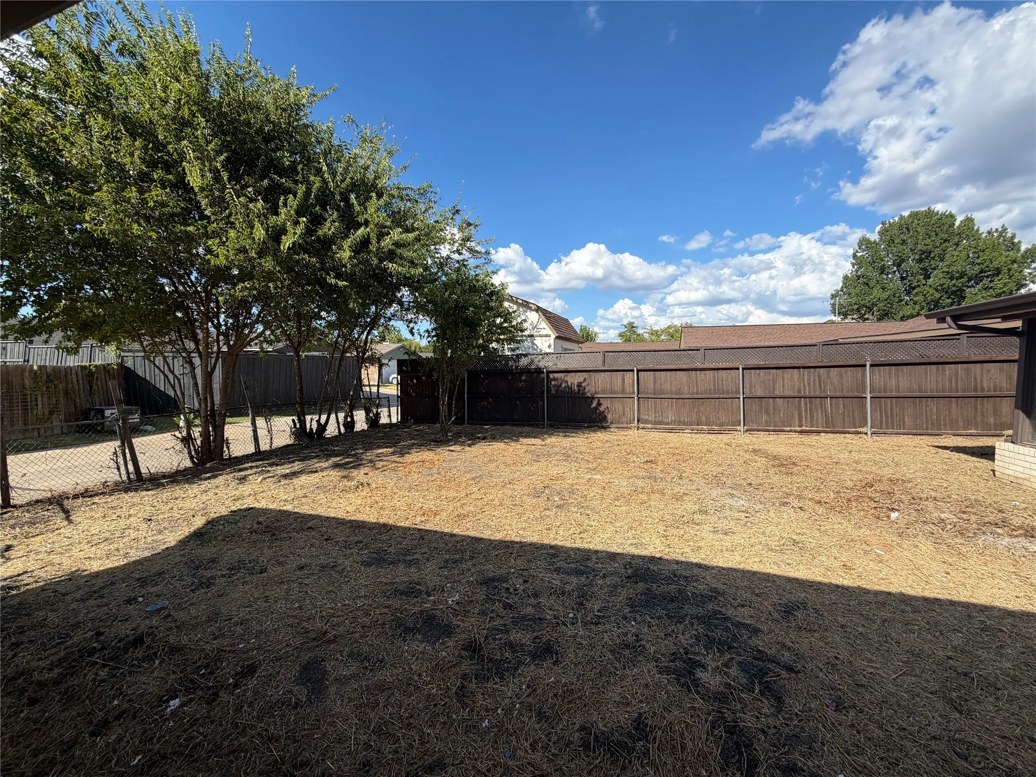 Expansive outdoor area featuring mature trees, a wood privacy fence, and a chain-link fence